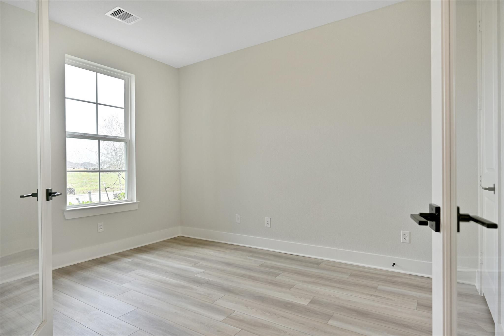 Empty bedroom with light laminate flooring, beige walls, large window, and open doors in Davidson Homes The Edward C, Lago Mar, Texas City