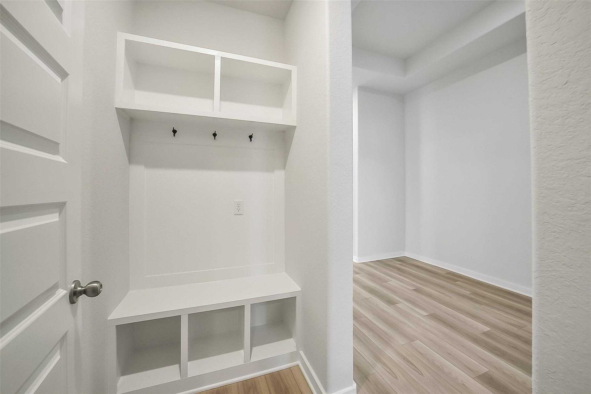 Modern white mudroom with built-in shelves, coat hooks, and storage bench in Davidson Homes The Acadia A, Sunterra, Katy