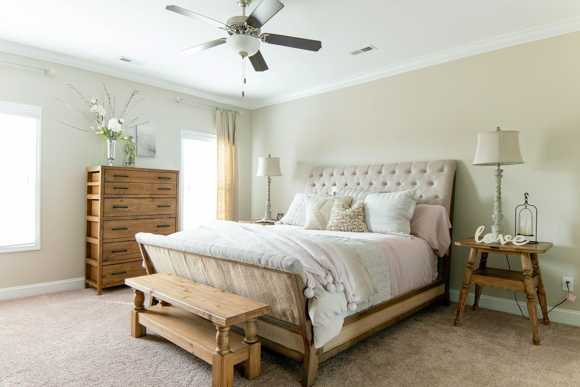 Spacious master bedroom at The Dairy at Oak Grove in South Huntsville AL with tufted upholstered bed, wooden dresser, and beige walls