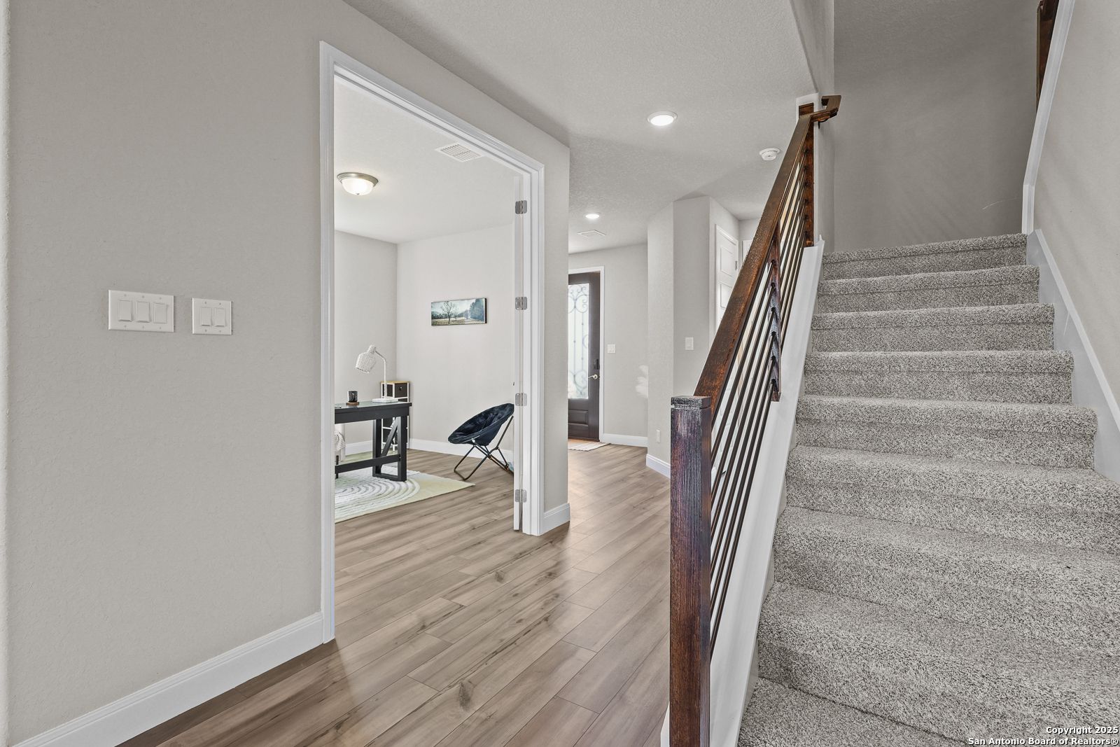 Elegant foyer with curved wooden staircase, metal railing, and adjacent home office in The Jennings G by Davidson Homes, Castroville, TX