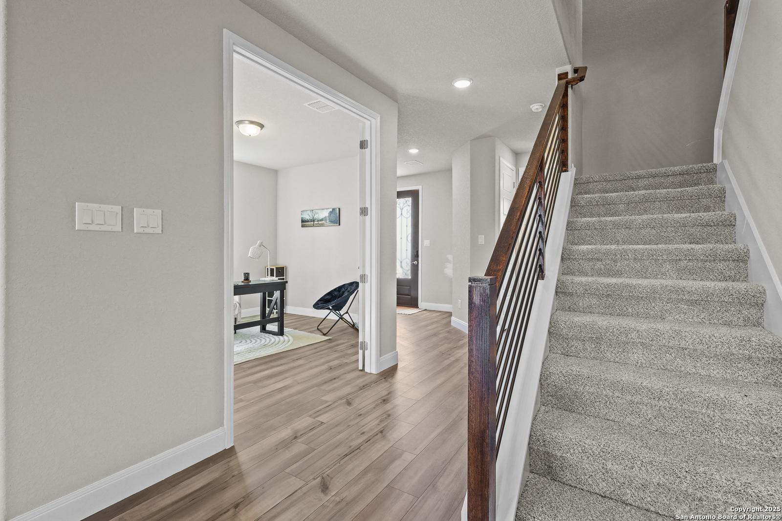 Elegant foyer with curved wooden staircase, metal railing, and adjacent home office in The Jennings G by Davidson Homes, Castroville, TX