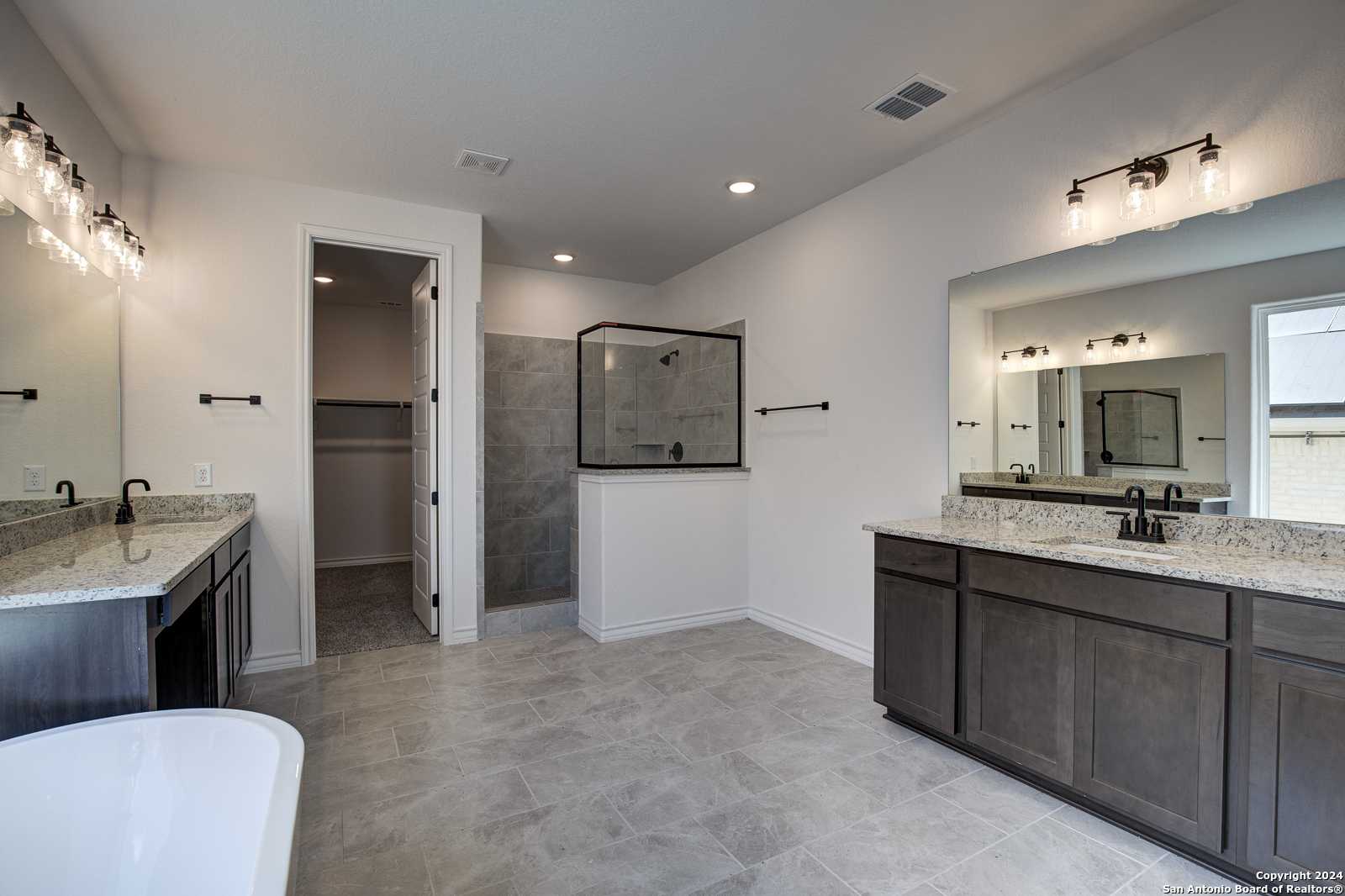 Modern master bathroom featuring double vanity, freestanding tub, walk-in shower, and dark cabinets in Davidson Homes The Garner B, Castroville, TX