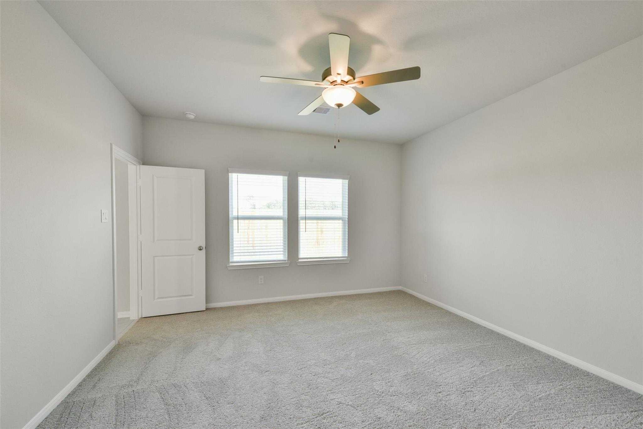 Bright secondary bedroom with ceiling fan, large windows, and carpeted flooring in The Sabine E home by Davidson Homes, Dayton, Texas
