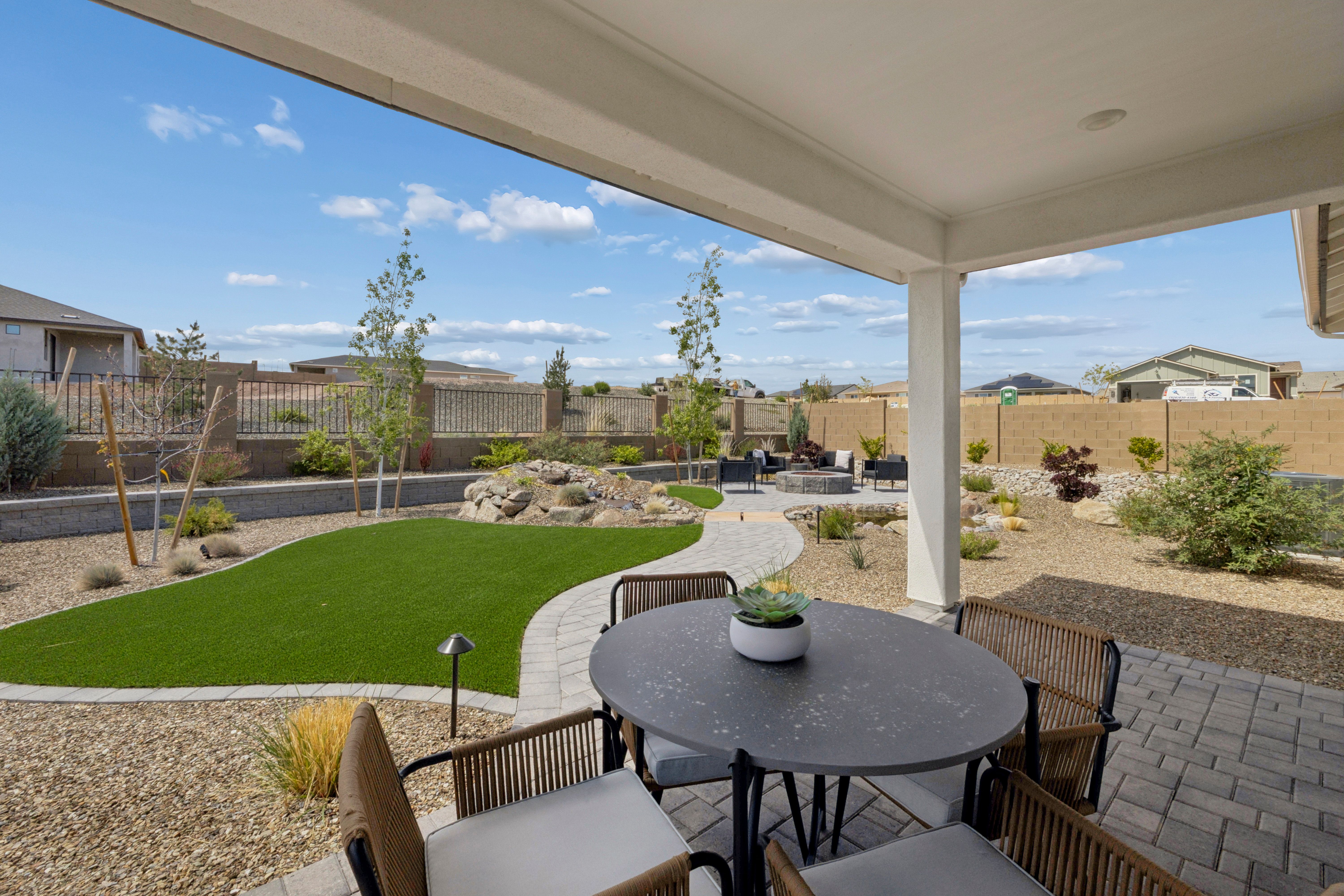 Covered patio with rattan dining set, artificial turf lawn, and desert rock landscaping at South Ranch Western Collection in Prescott AZ