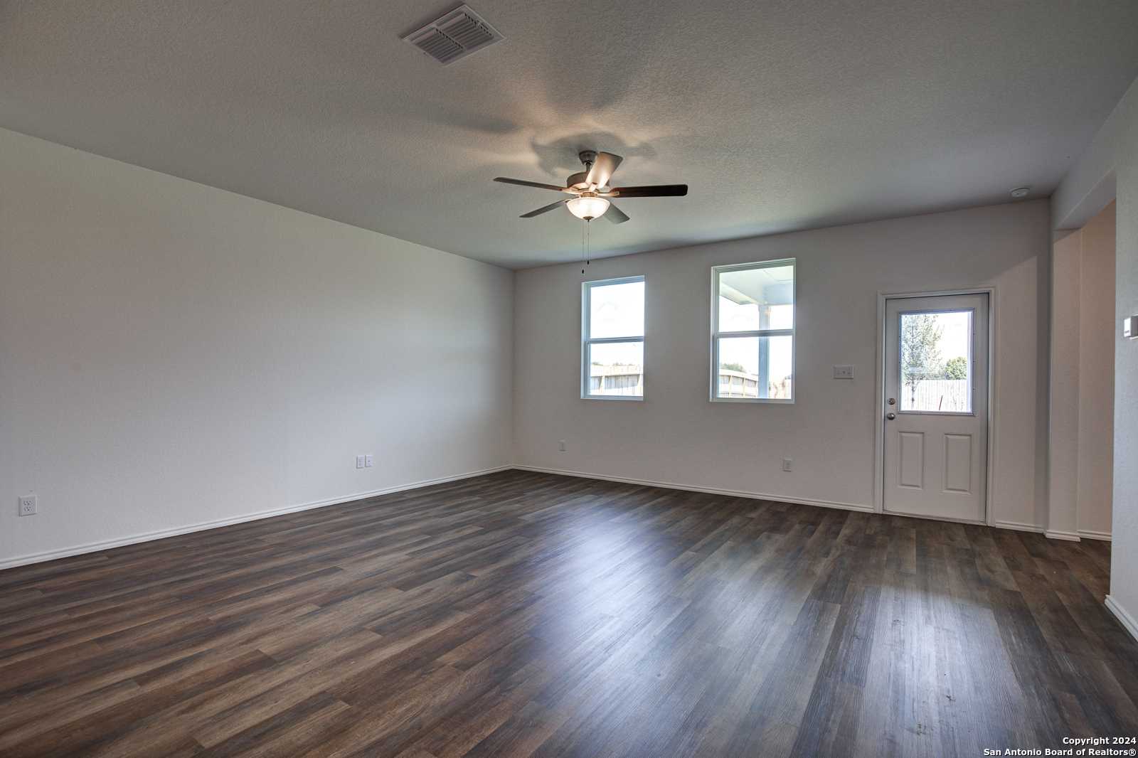 Spacious living room with hardwood floors, ceiling fan, and large windows in Davidson Homes The Douglas D, Seguin, Texas
