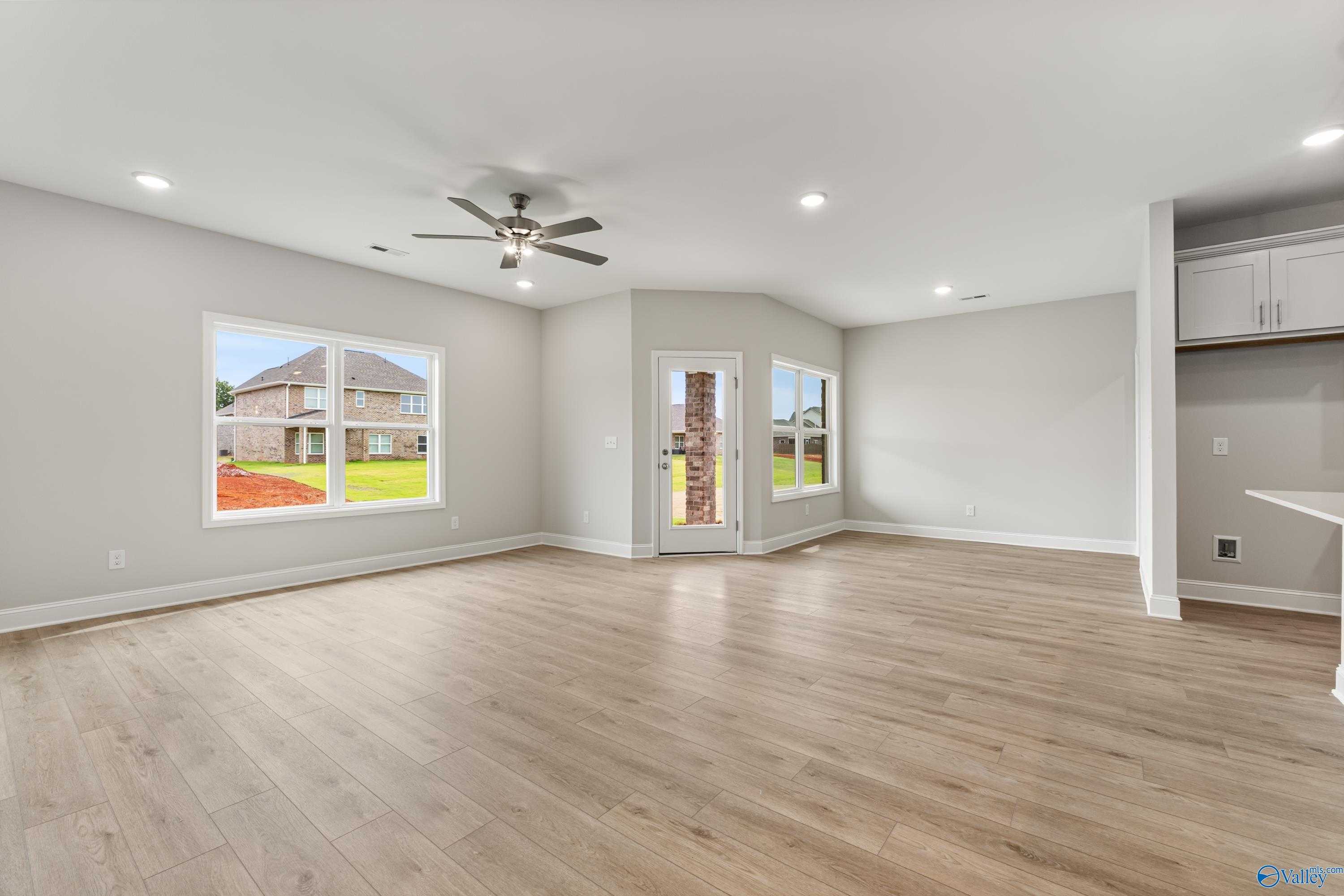 Spacious living room with hardwood floors, gray walls, ceiling fan, and large windows overlooking green backyard in The Daphne C home, Athens, Alabama