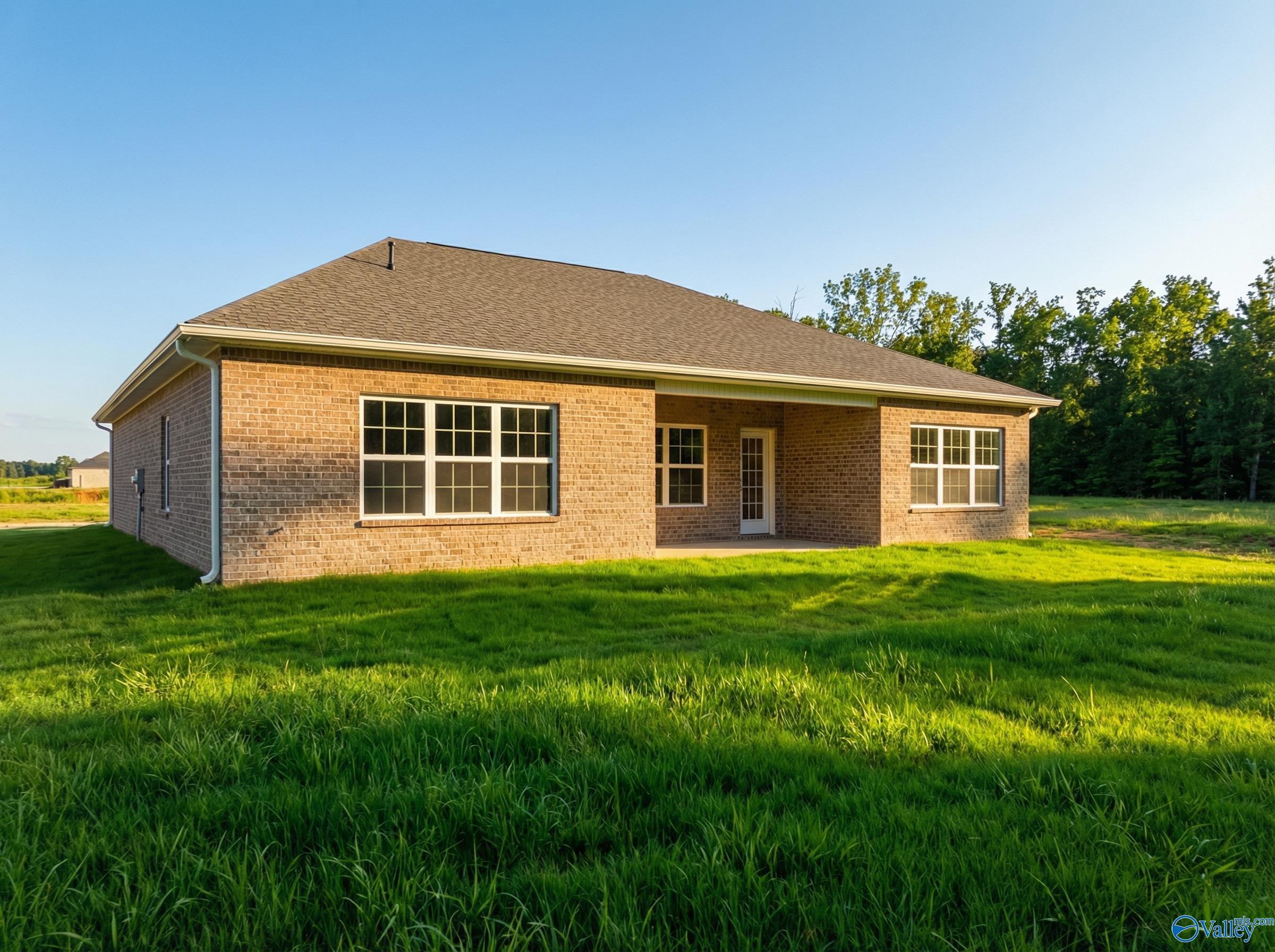 Single-story brick home with gabled roof, covered patio, large windows, lush green lawn, and trees in Cain Park, Hartselle, Alabama