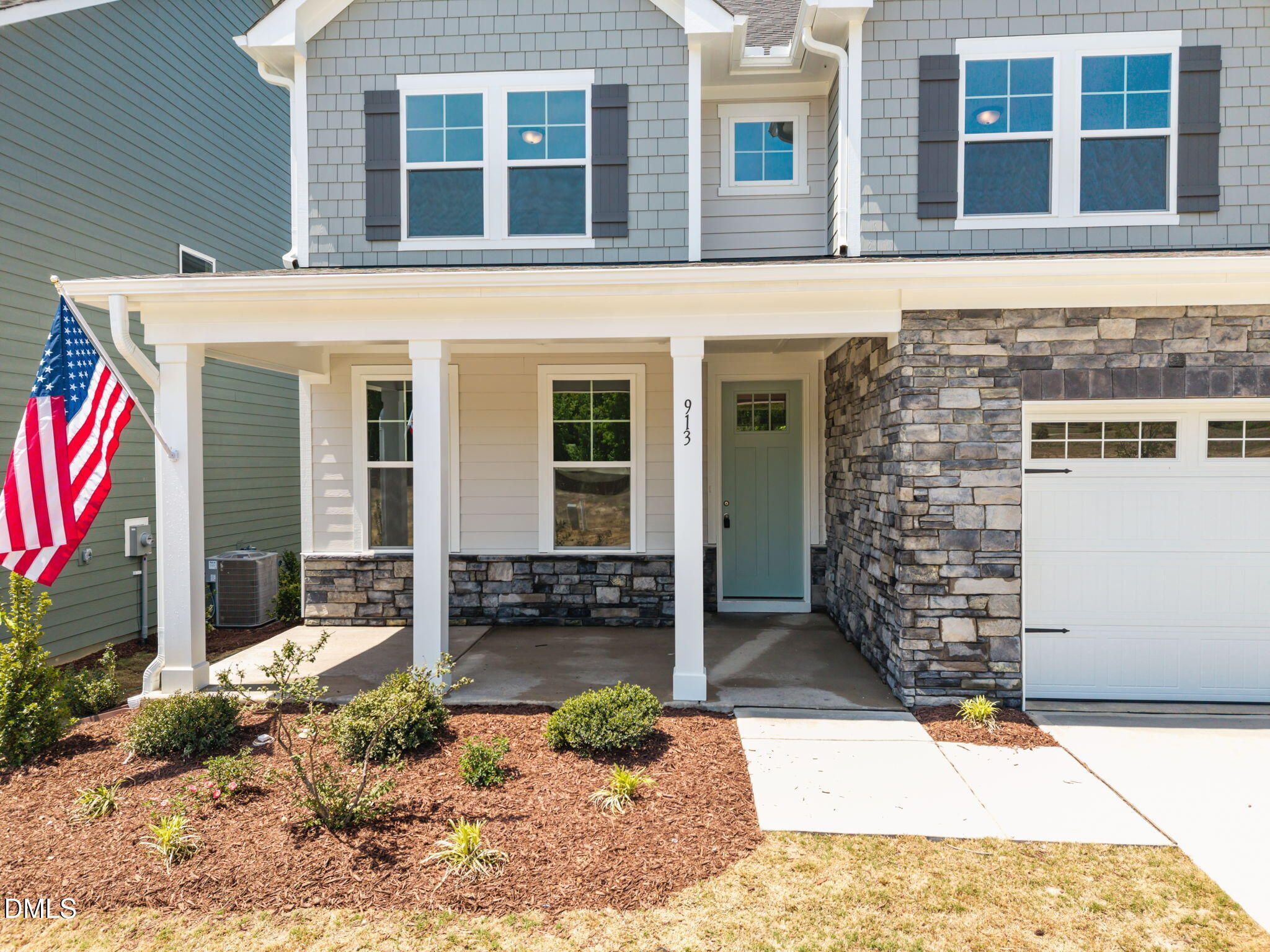 Modern two-story gray home with covered porch, turquoise door, stone garage, American flag, and landscaped front yard in Wendell, NC