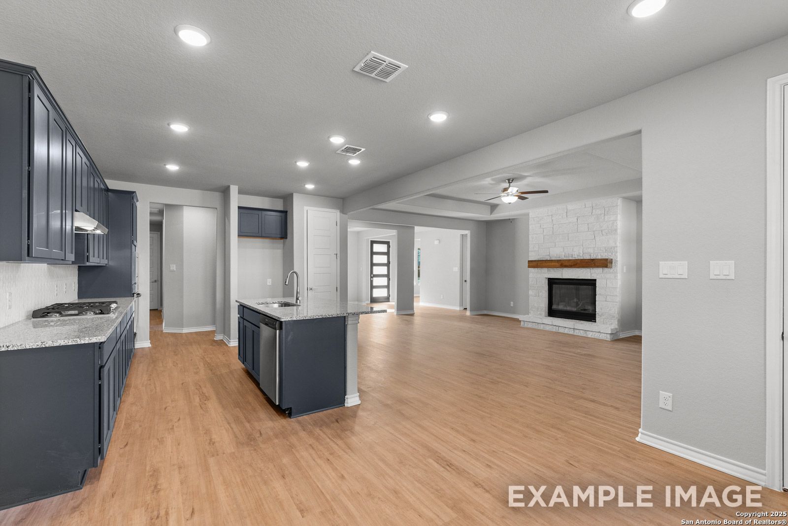 Open-concept kitchen and living area in The Oxford H featuring navy cabinets, stone fireplace, and wood-style flooring.