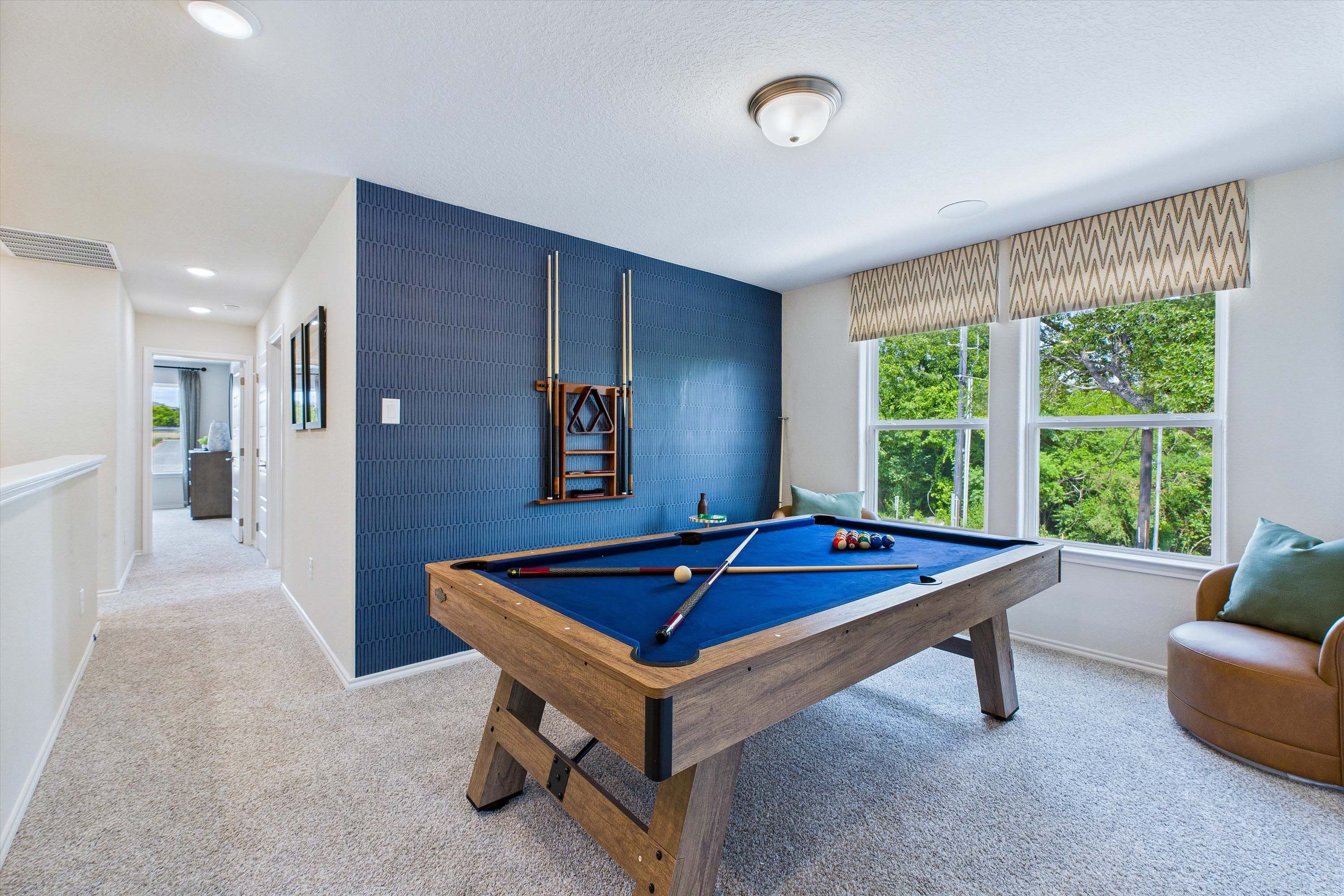 Spacious game room in The Gillian C featuring a pool table, vibrant blue accent wall, and cozy lounge seating.