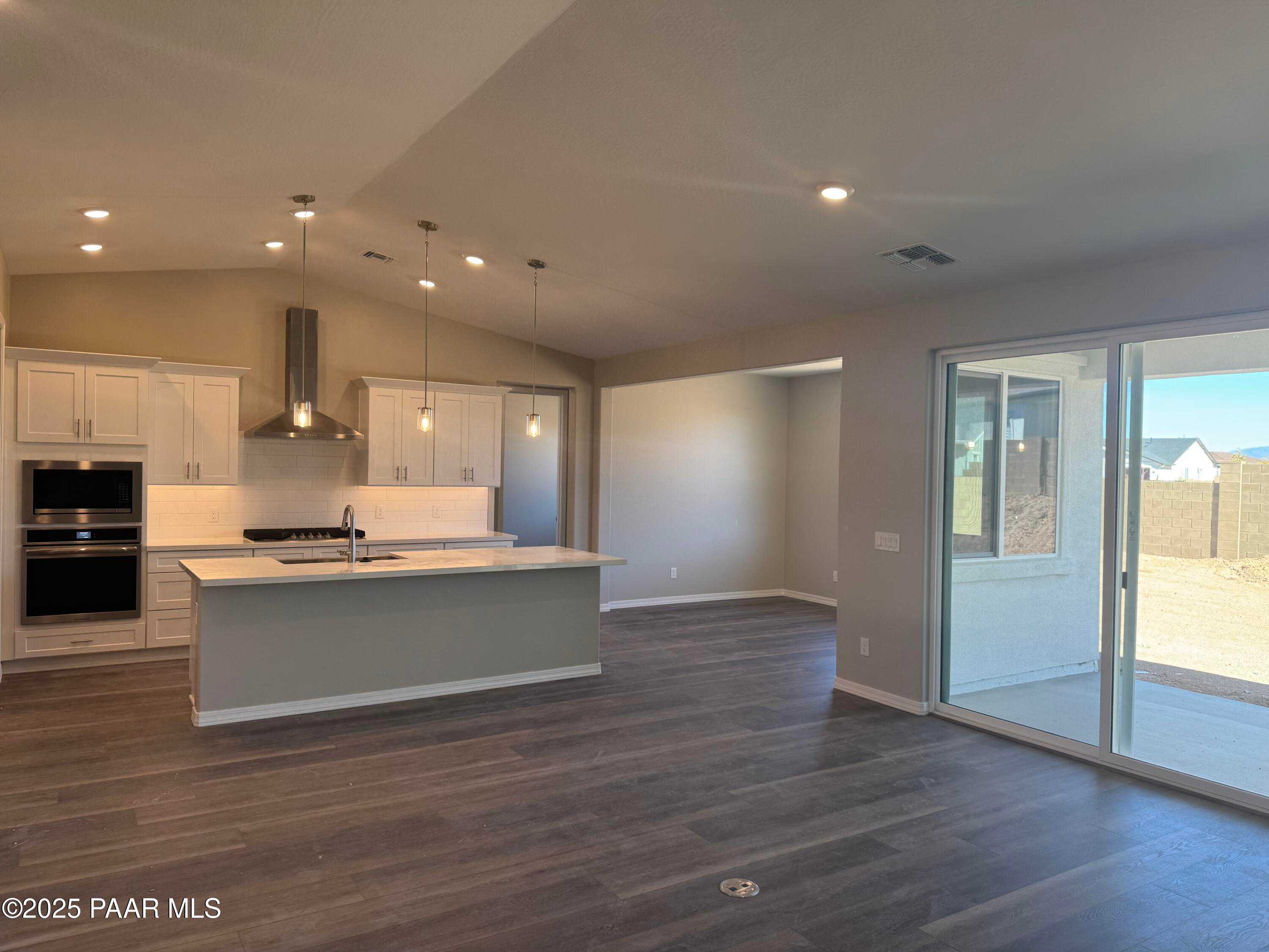 Modern open-concept kitchen with white cabinets, stainless steel appliances, large island, and sliding doors to desert view in The Monarch E, Prescott, AZ