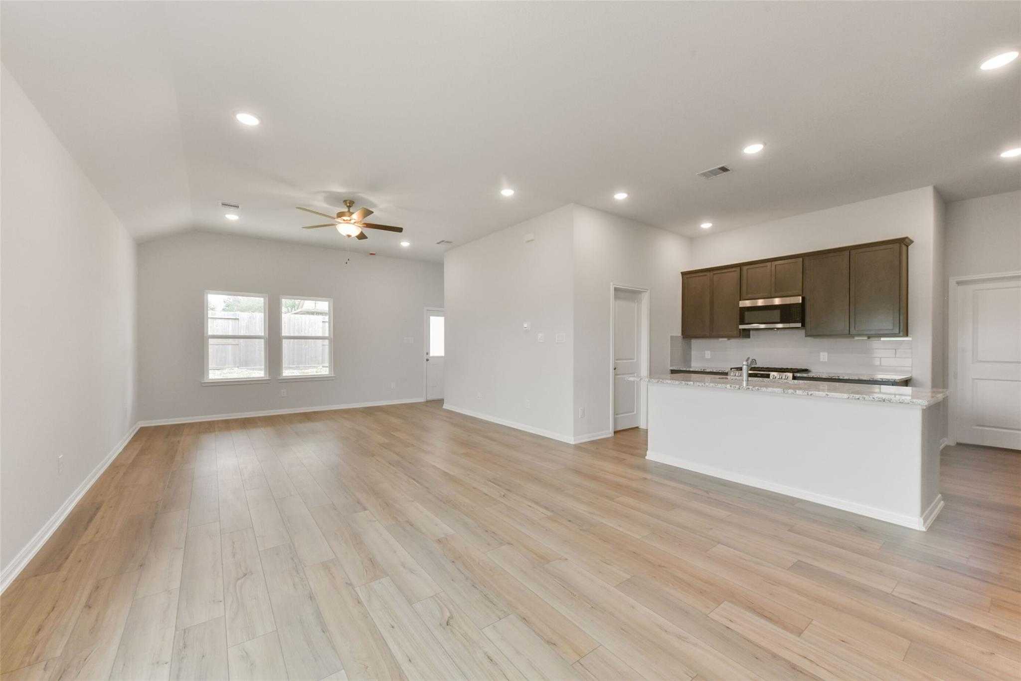 Open-concept living room and kitchen with vaulted ceiling, ceiling fan, large windows, and white island cabinets in Davidson Homes The Laguna B, Magnolia Texas
