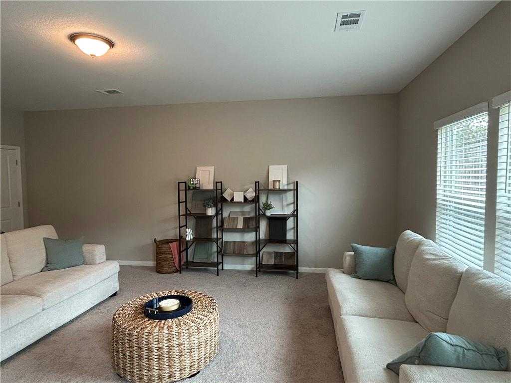 Cozy living room with neutral beige walls, plush sofas, wicker coffee table, and metal shelving in Davidson Homes The Bartlett, Phenix City, Alabama