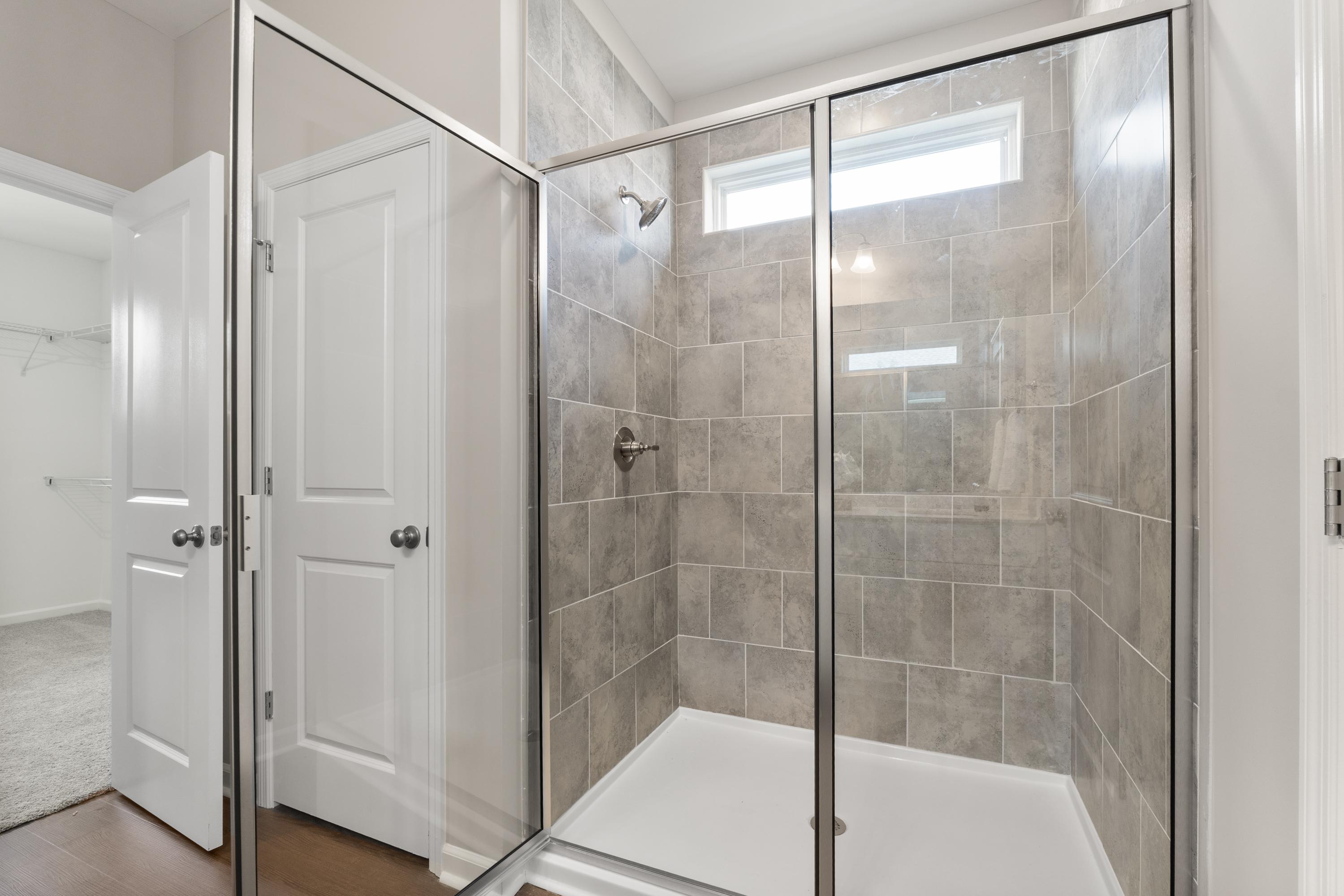 Spacious master shower in The Avalon D with frameless glass enclosure, gray subway tile, rainfall head, and clerestory window