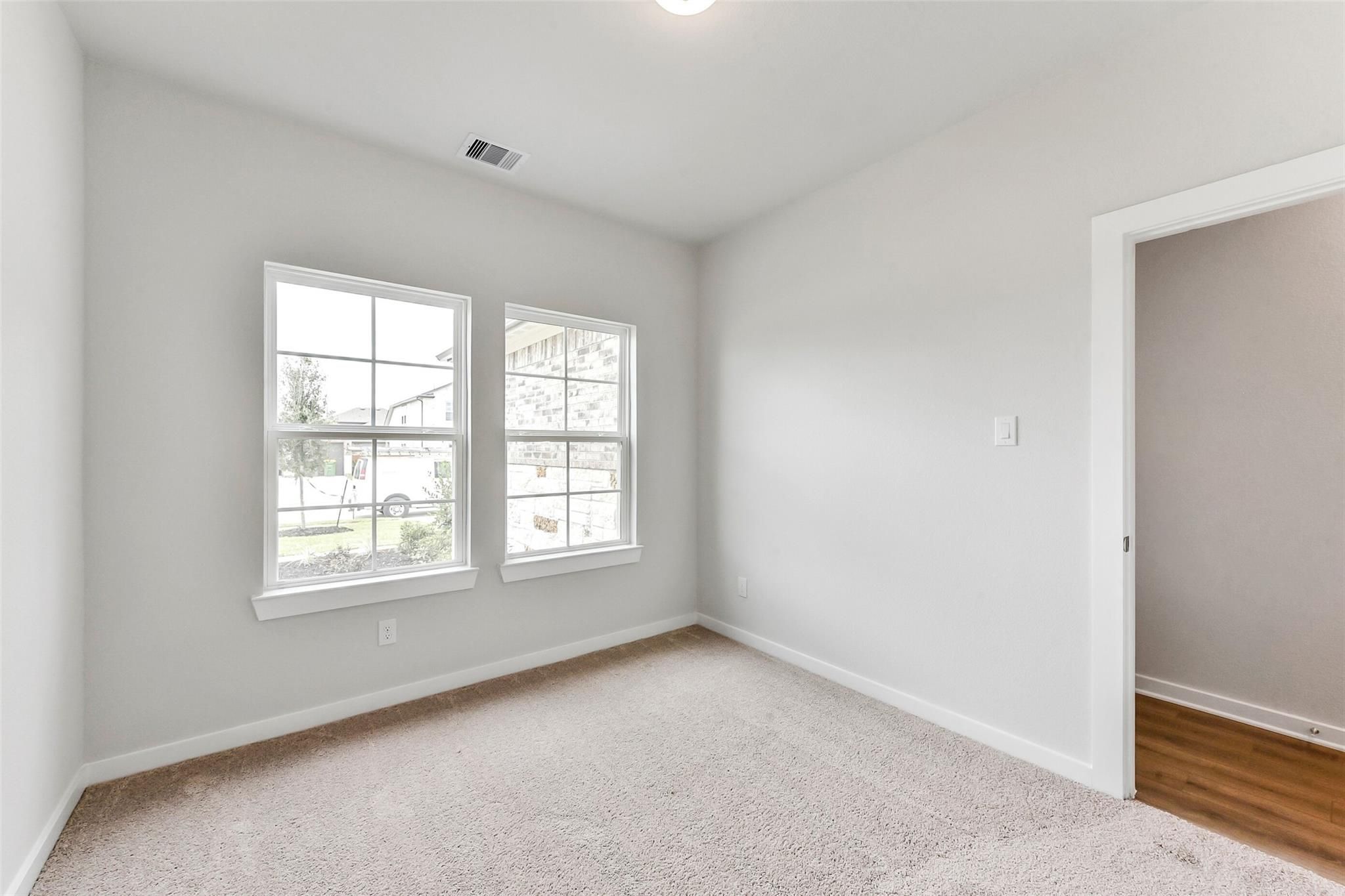 Bright secondary bedroom with large windows, neutral gray walls, and plush carpet in Davidson Homes The Costa B, Dayton, Texas