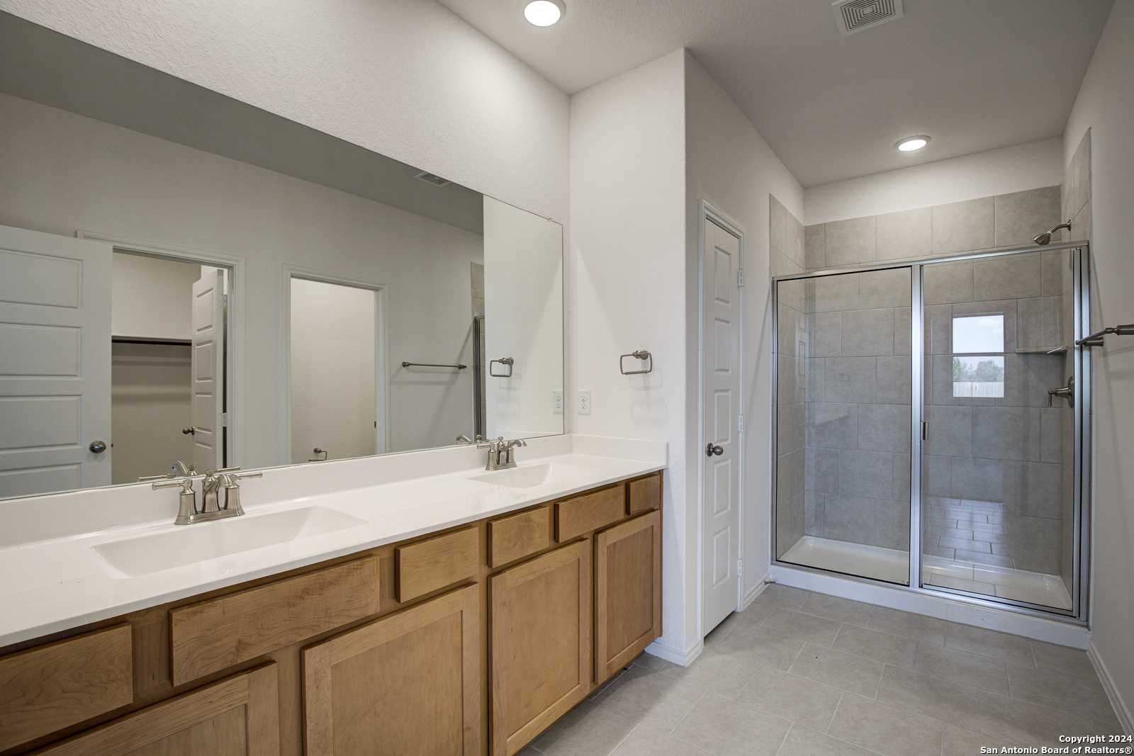 Modern master bathroom with double vanity sinks, walk-in glass shower, and shaker cabinets in Davidson Homes The Douglas D, Seguin, Texas