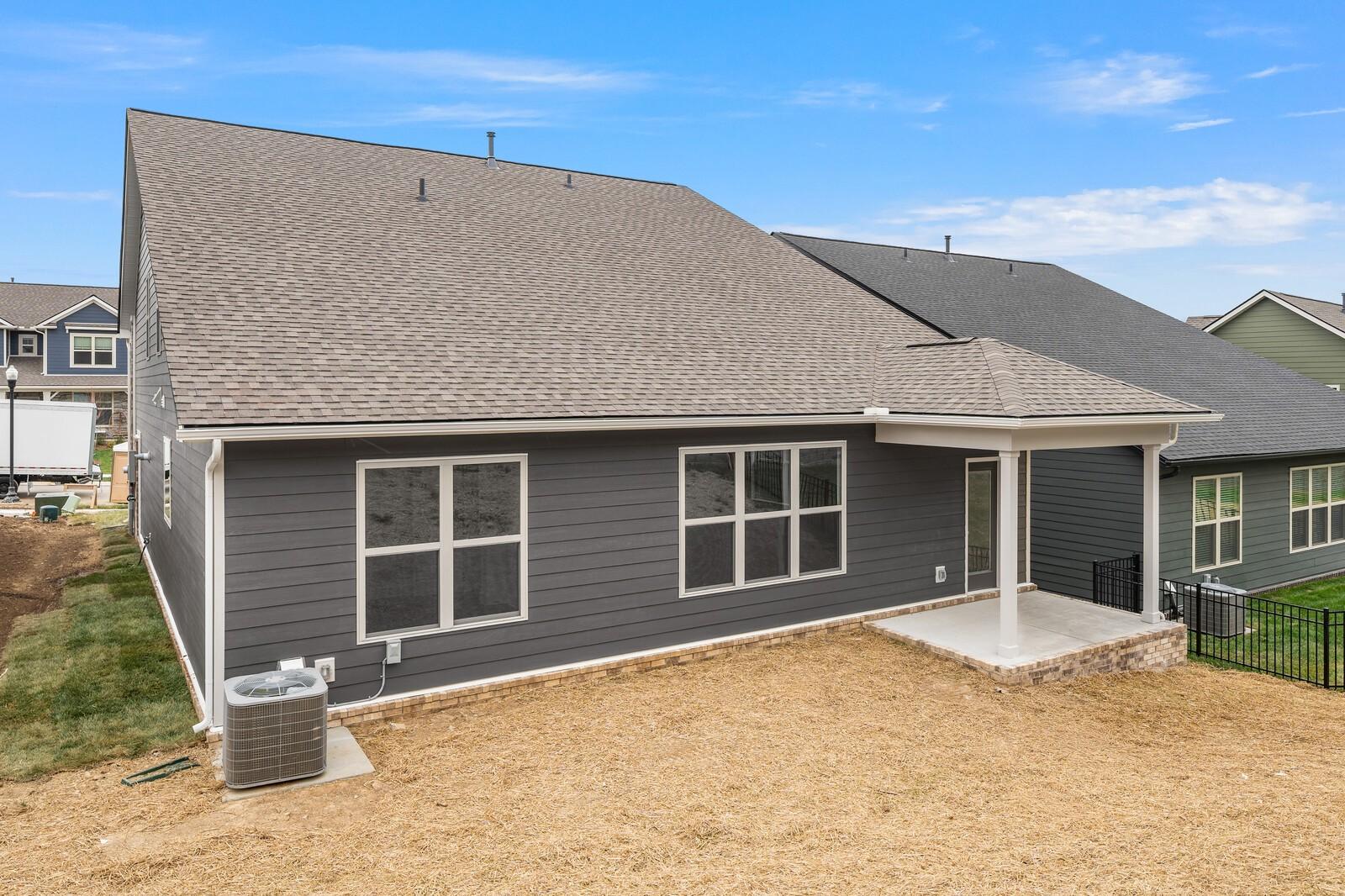 Rear view of gray two-story Ridgeport C home with covered patio, windows, and gravel backyard in Woods Crossing, Gallatin, Tennessee