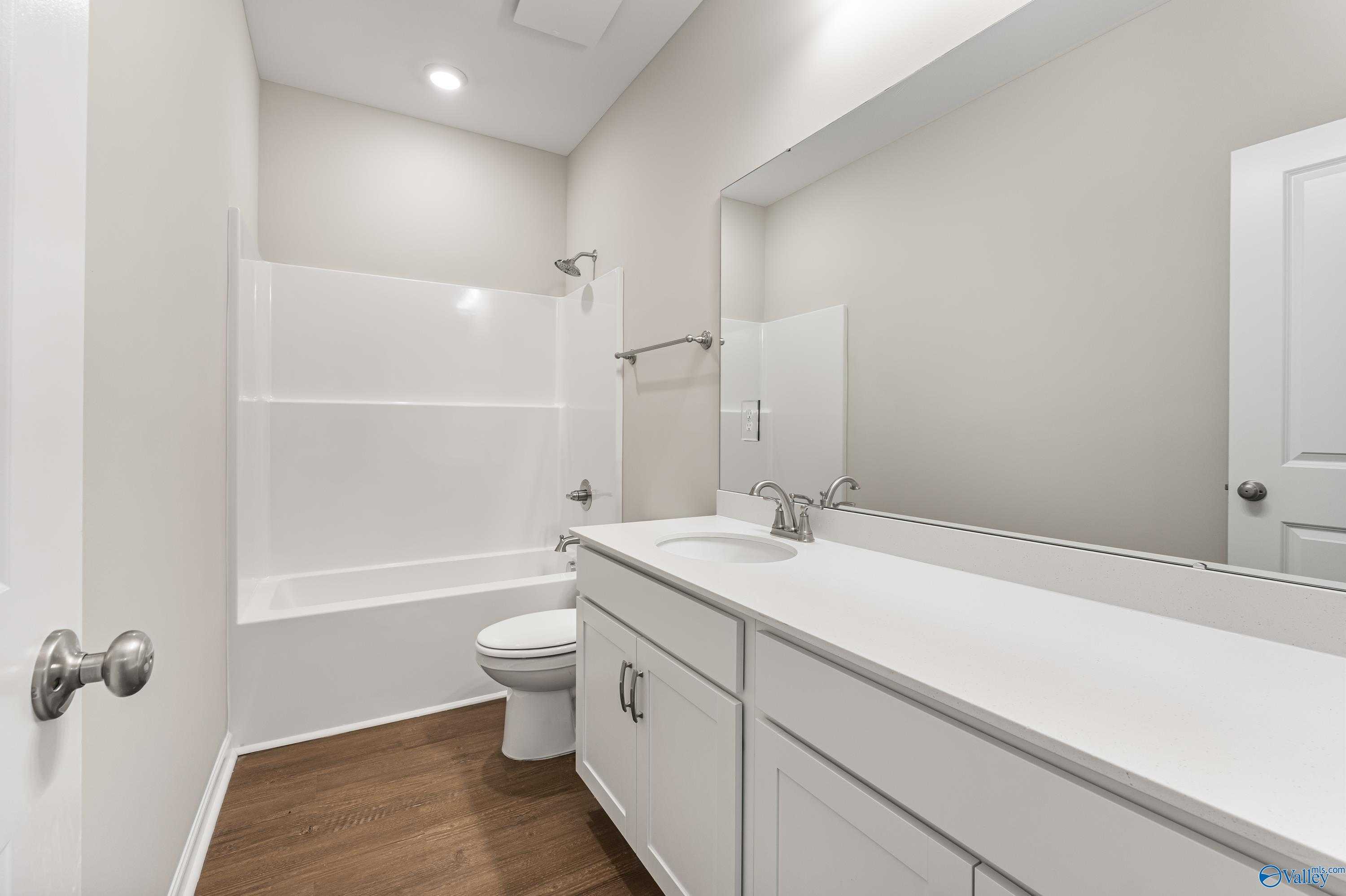 Modern bathroom with white tub-shower combo, single vanity sink, toilet, and hardwood floors in Davidson Homes The Phoenix, Fayetteville, TN
