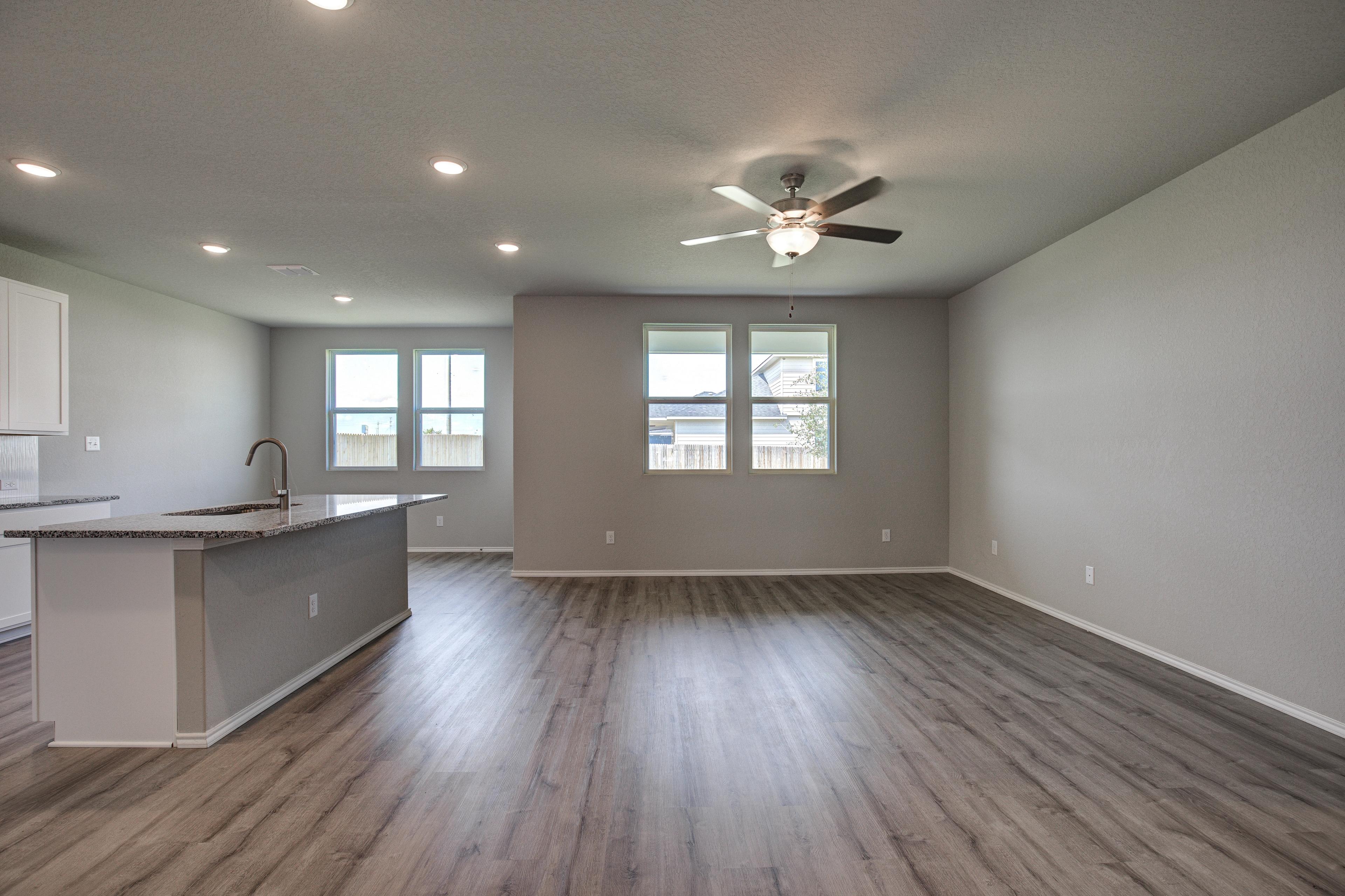 Spacious open-concept kitchen and living room in The Asheville with gray island, large windows, ceiling fan, and hardwood floors