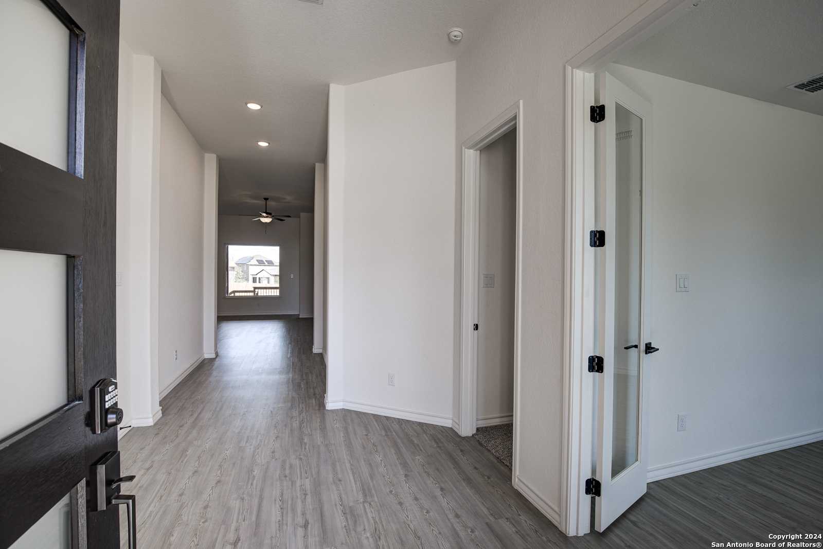 Bright entryway with open hallway, gray laminate floors, white walls, and ceiling fan in The Garner B home, Castroville, Texas
