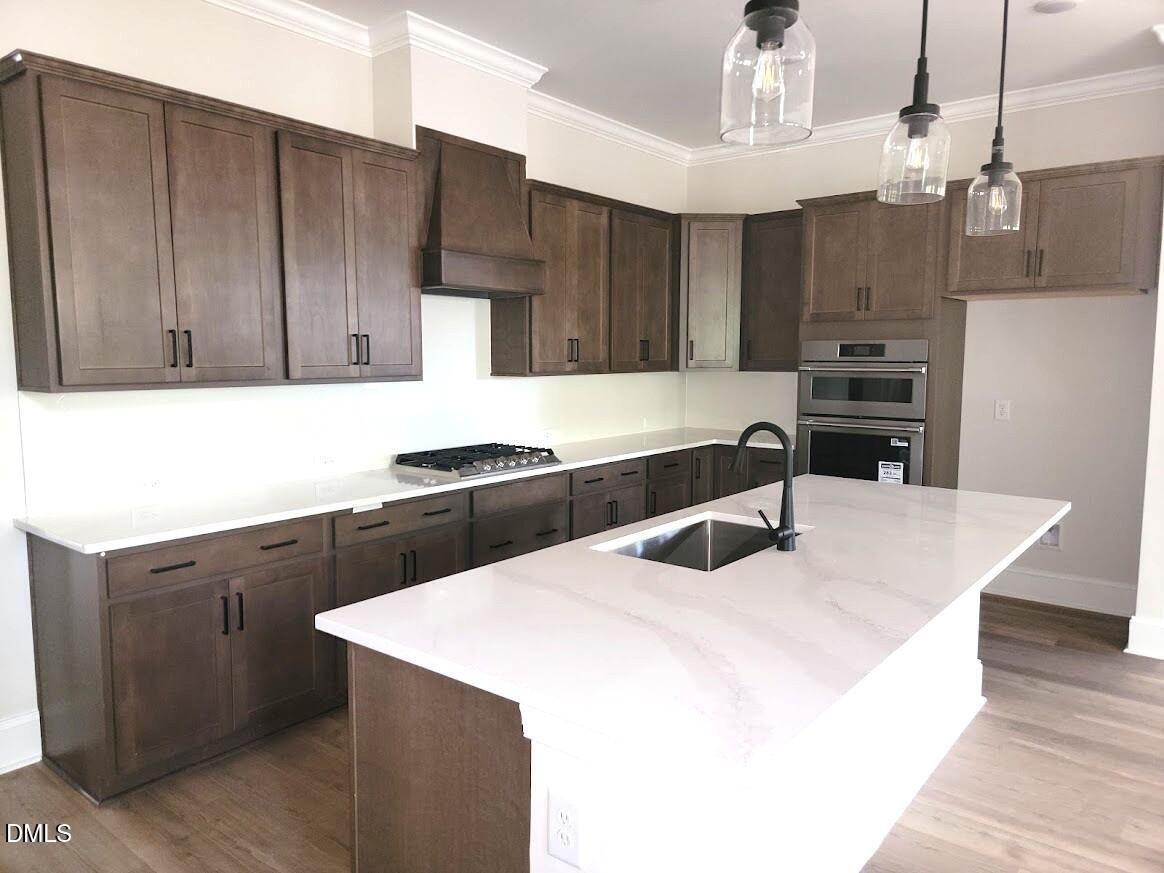 Kitchen island with white quartz countertops, dark wood cabinets, and pendant lighting in Davidson Homes Magnolia II B, Wake Forest NC