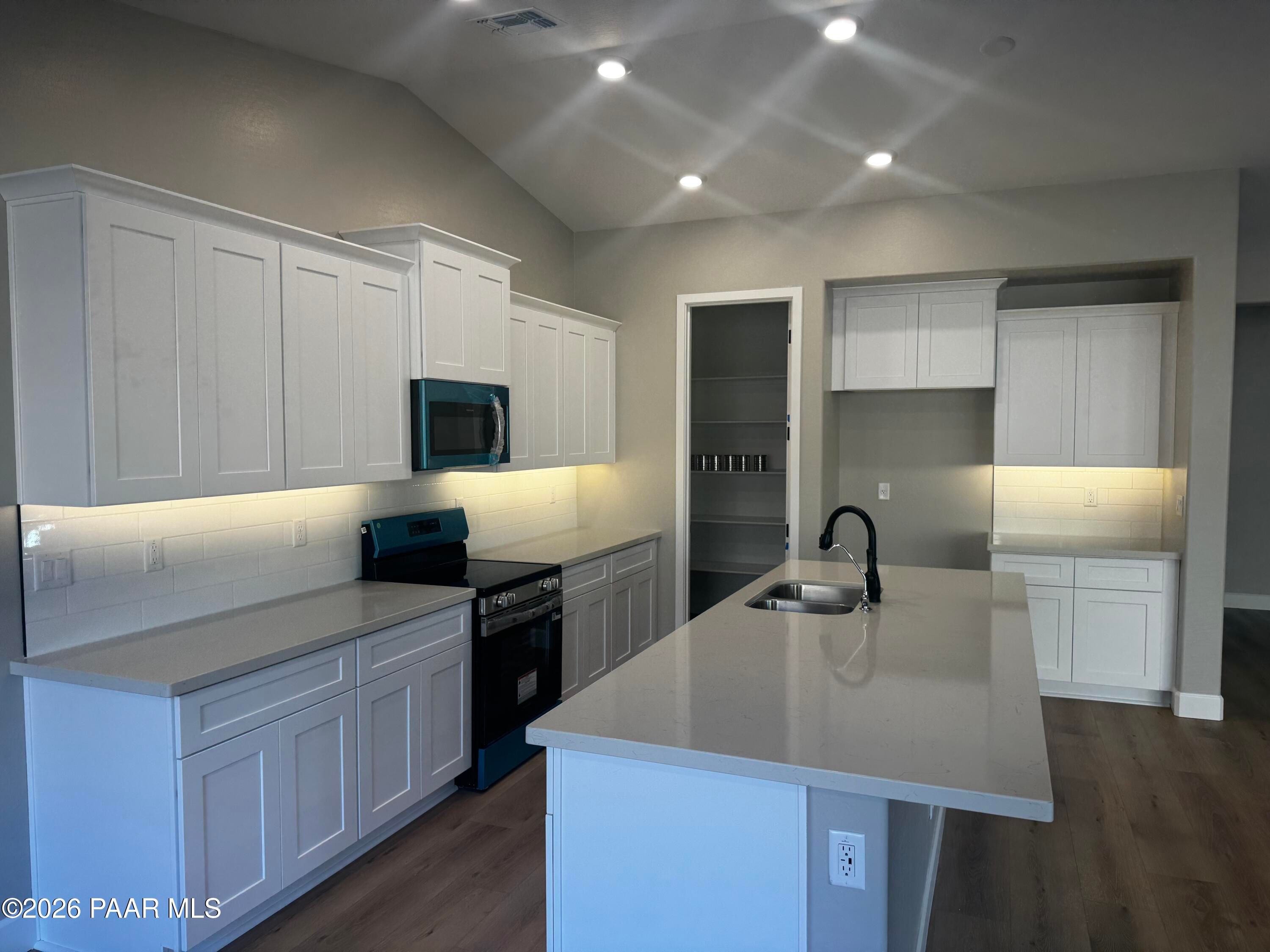 Modern kitchen with white shaker cabinets, quartz island sink, and recessed lighting in Evermore Homes The Monarch B, Prescott Valley, AZ