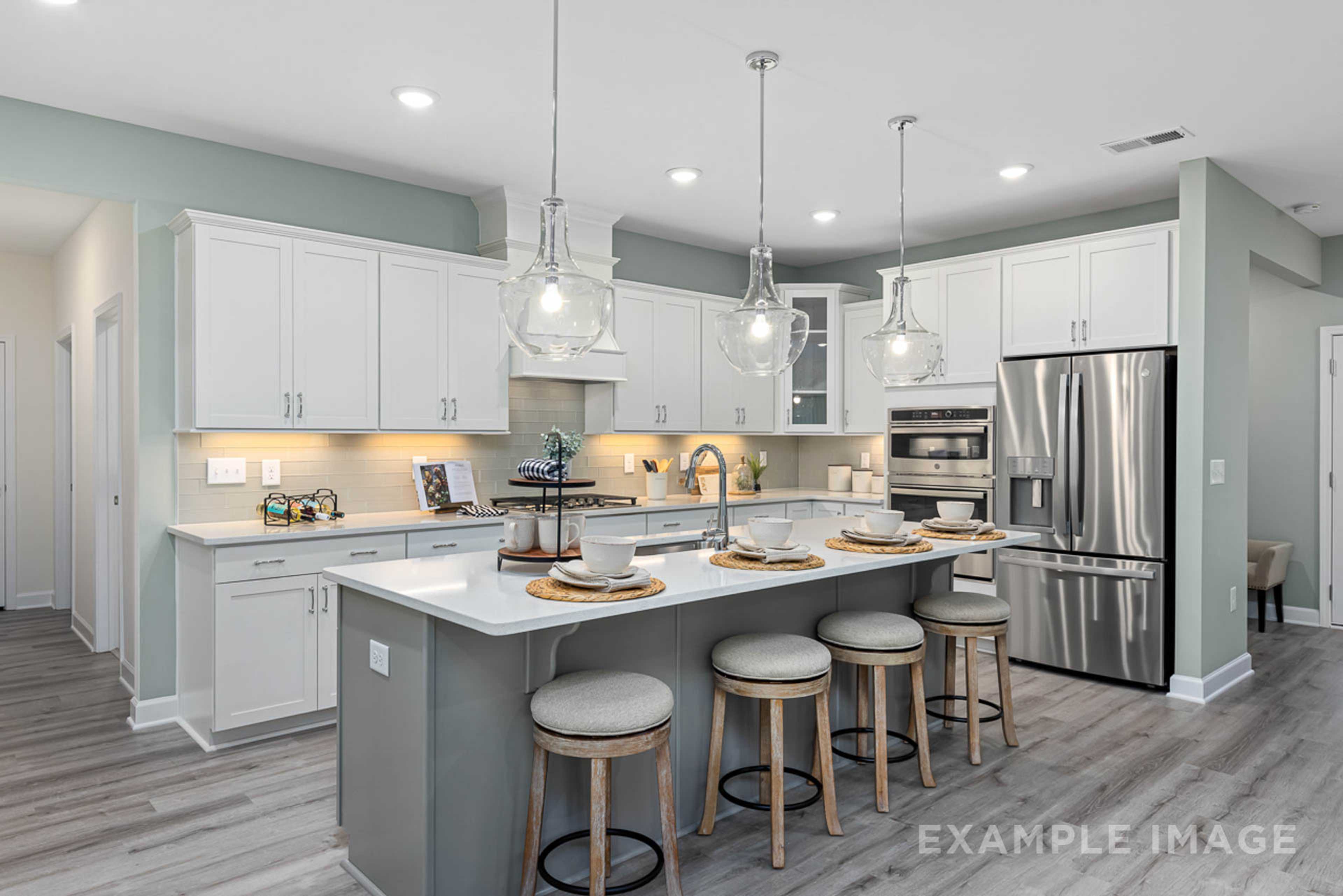 Modern open-concept kitchen in Windgate, Mooresville NC with white shaker cabinets, gray island, bar stools, stainless steel appliances, and hardwood floors