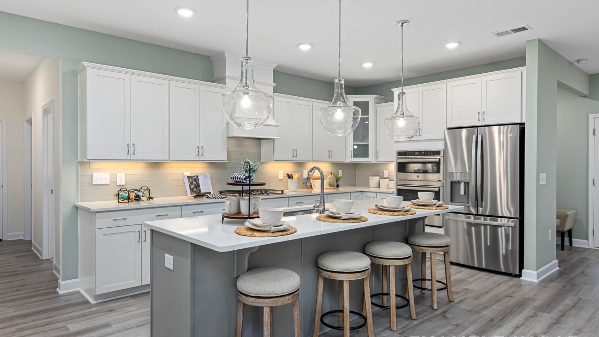 Modern open-concept kitchen in Windgate, Mooresville NC with white shaker cabinets, gray island, bar stools, stainless steel appliances, and hardwood floors