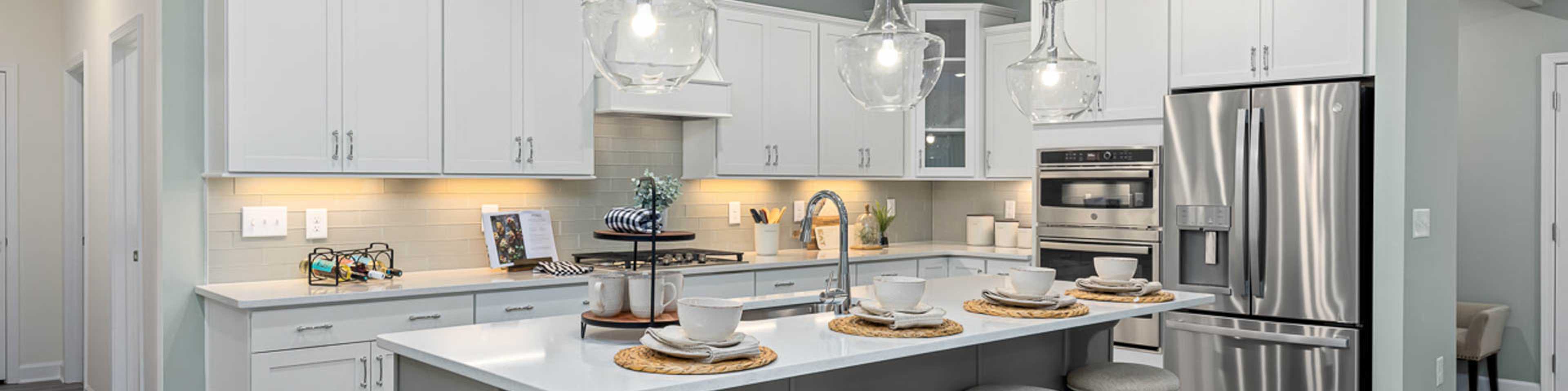 Modern open-concept kitchen in Windgate, Mooresville NC with white shaker cabinets, gray island, bar stools, stainless steel appliances, and hardwood floors