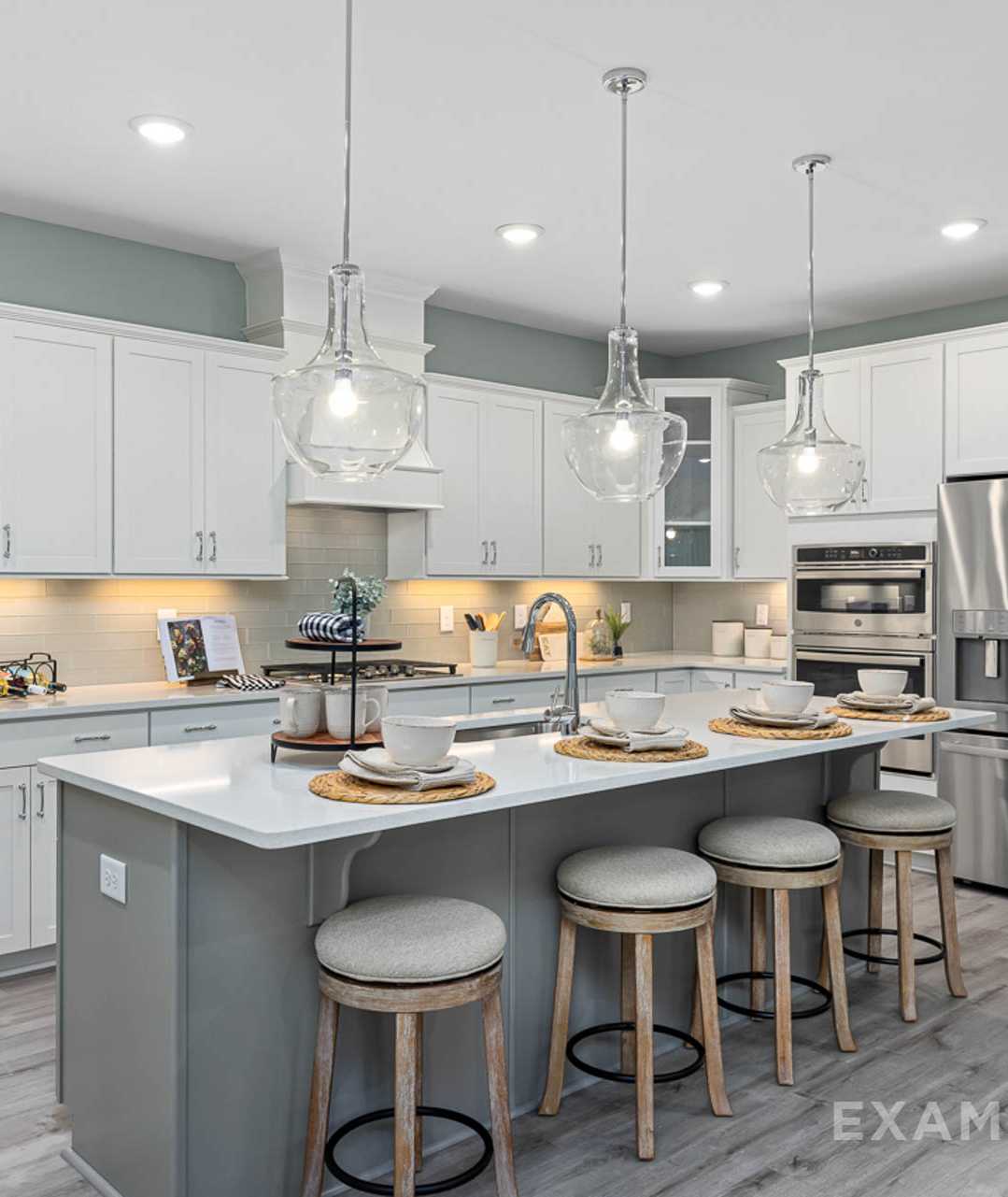 Modern open-concept kitchen in Windgate, Mooresville NC with white shaker cabinets, gray island, bar stools, stainless steel appliances, and hardwood floors