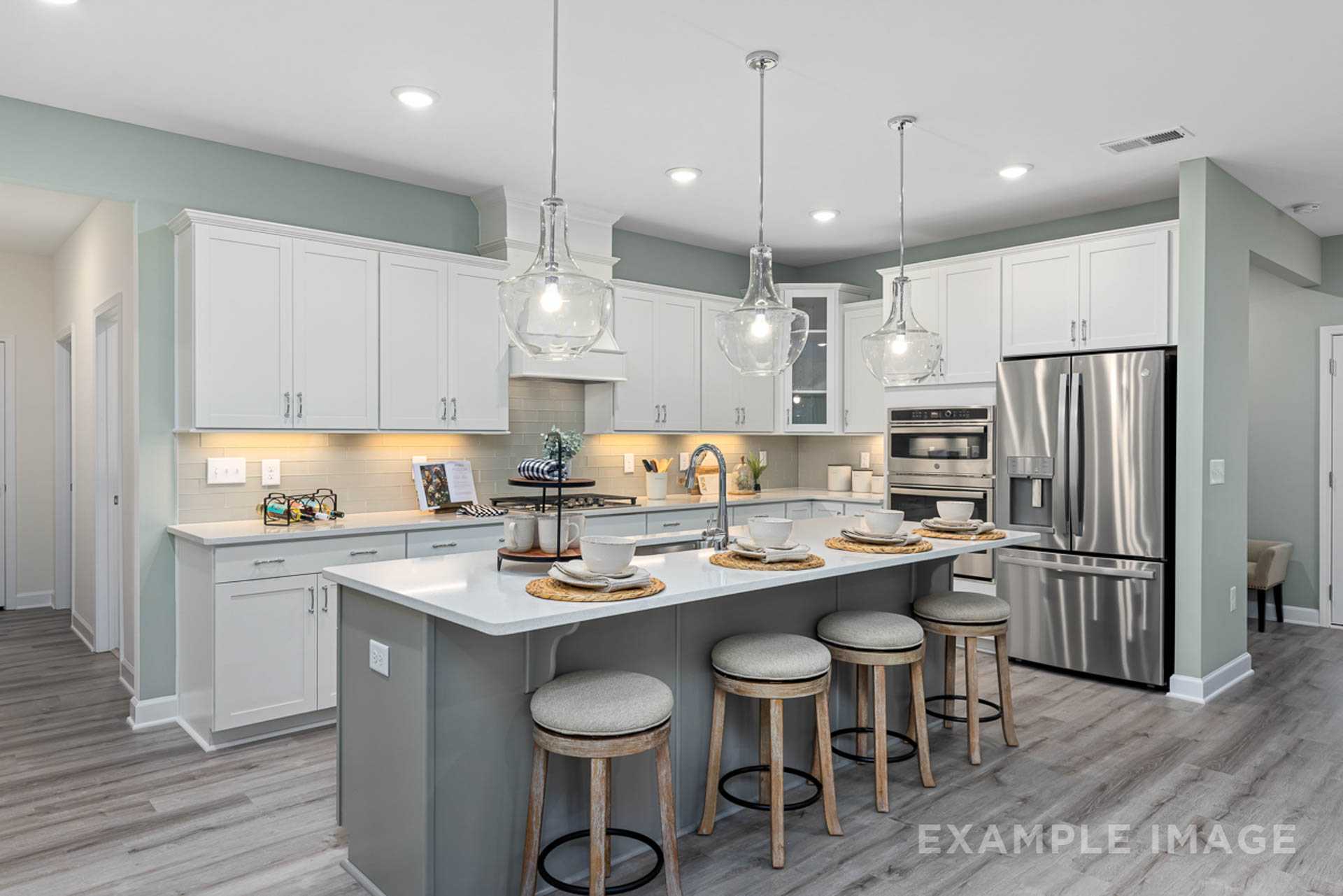 Modern open-concept kitchen in Windgate, Mooresville NC with white shaker cabinets, gray island, bar stools, stainless steel appliances, and hardwood floors