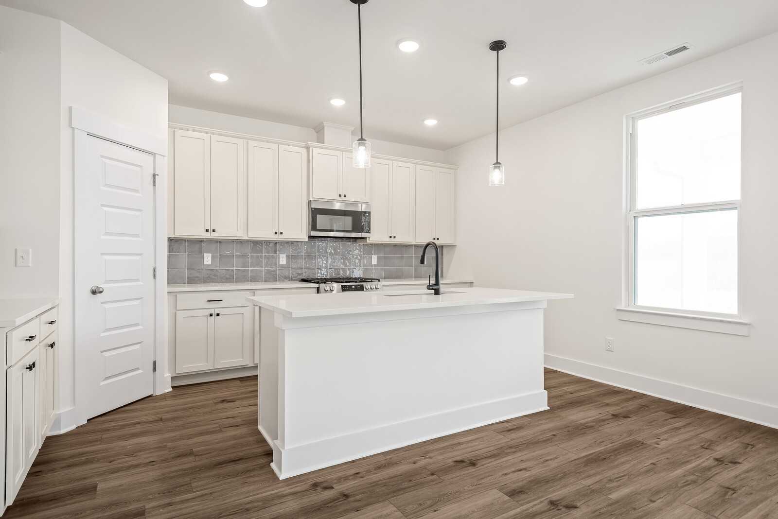 Modern white kitchen featuring large island, stainless appliances, subway tile backsplash, and pendant lights in The Logan C, Gallatin, TN