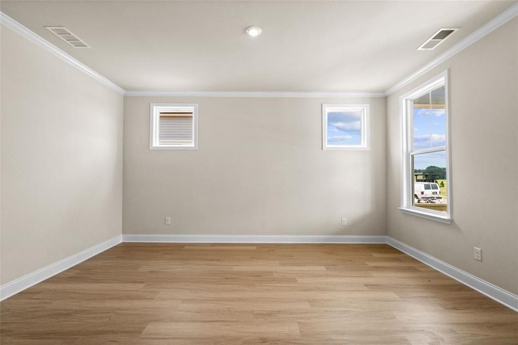 Empty bedroom with hardwood floors, beige walls, and large windows in Davidson Homes The Hickory B at Wehunt Meadows, Hoschton, Georgia