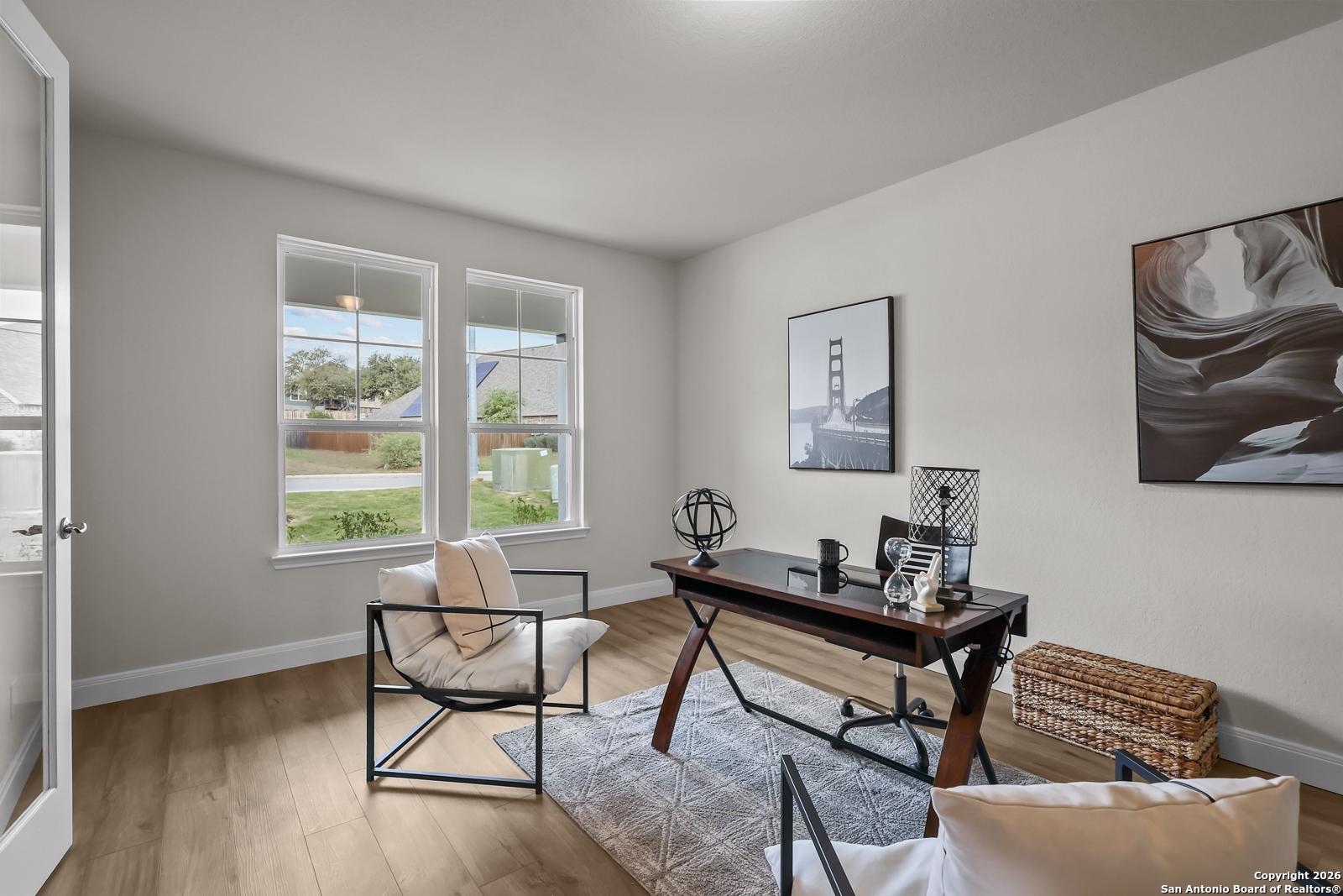 Elegant home office with wooden desk, black metal chairs, abstract wall art, and garden views in Davidson Homes The Lanier H, Ladera, San Antonio
