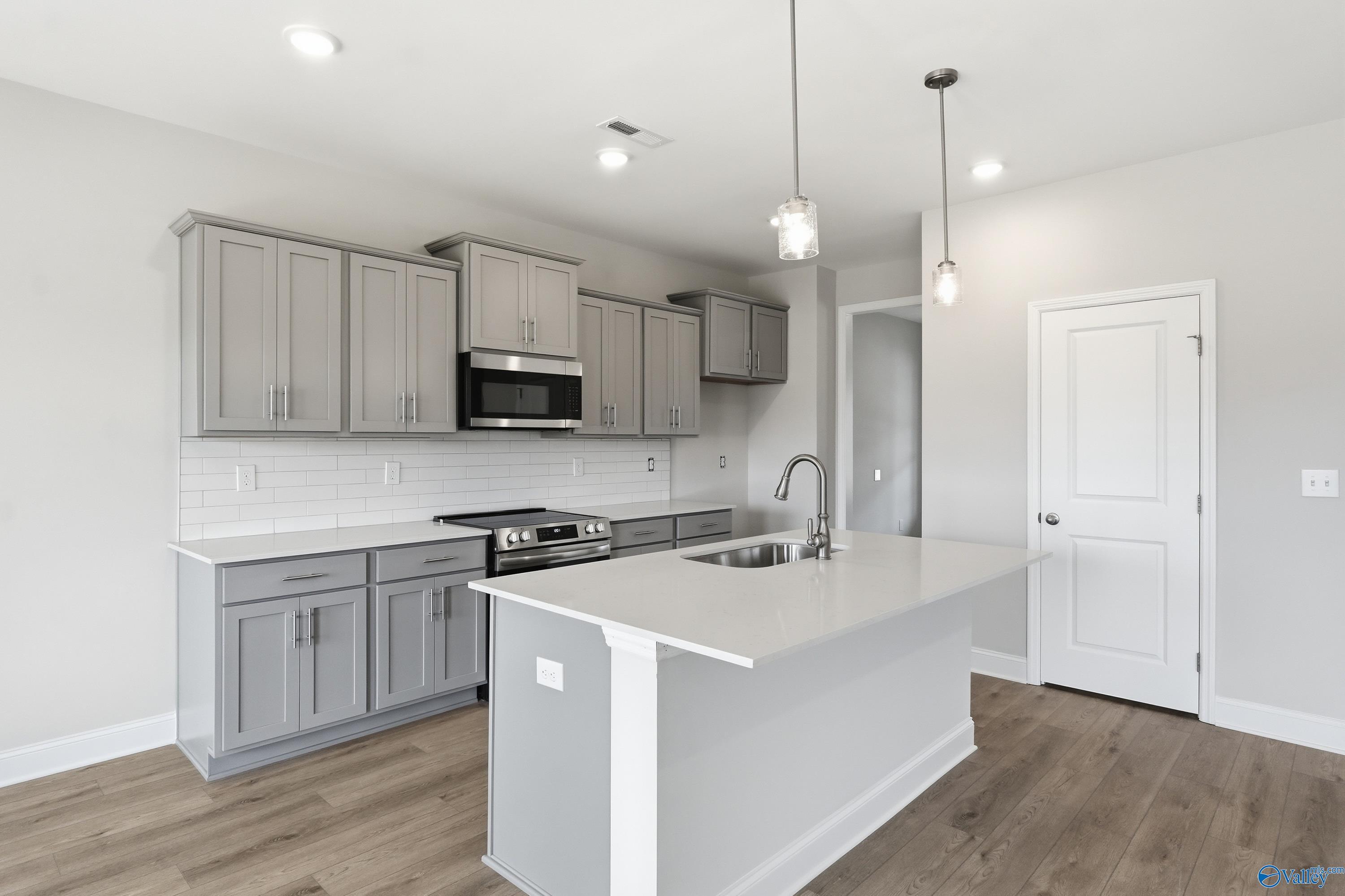 Modern gray shaker kitchen with white quartz island, stainless appliances, subway tile backsplash in Davidson Homes Shelby B, New Market AL