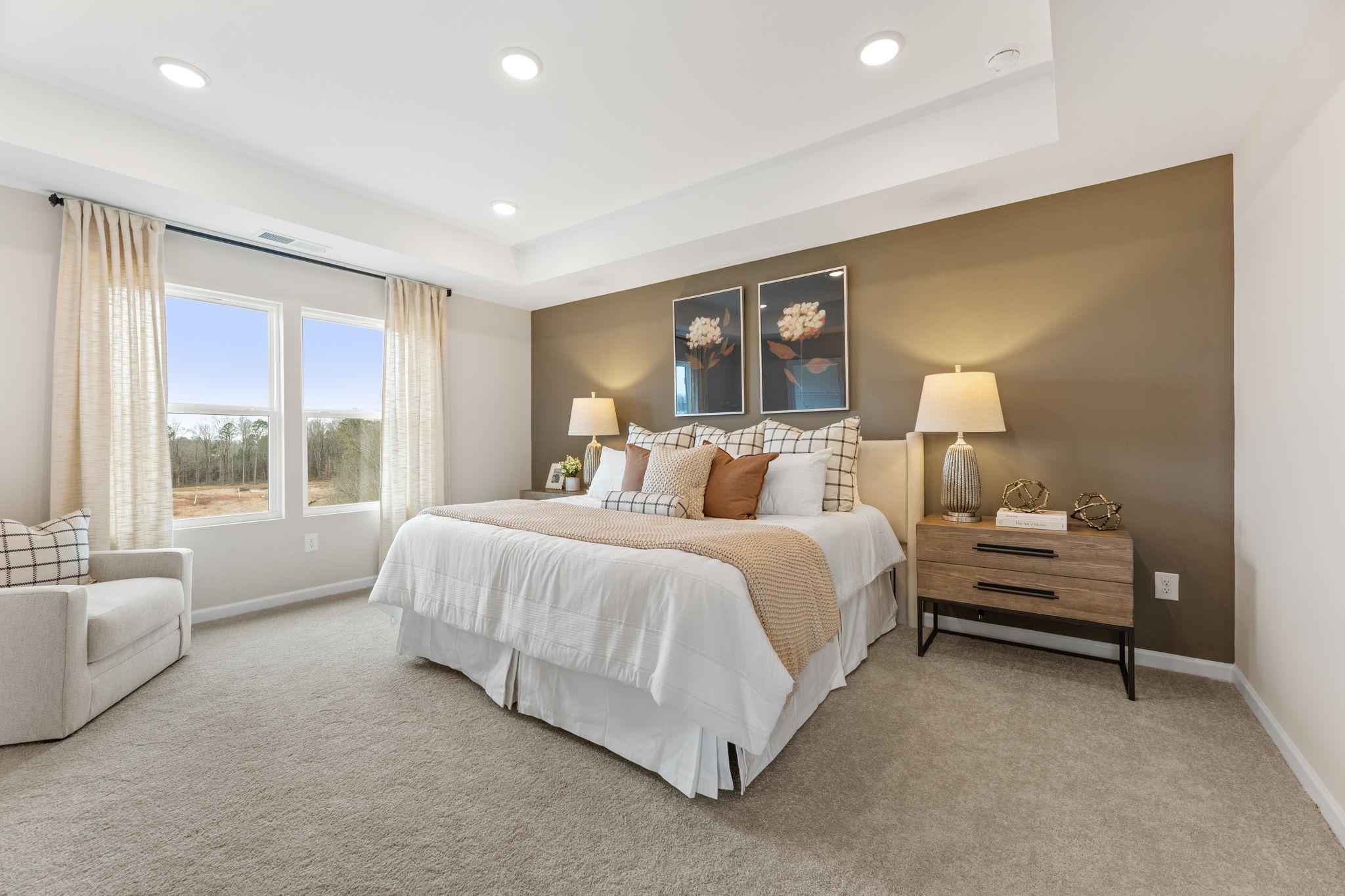 Elegant master bedroom with king bed, neutral pillows, beige walls, large windows overlooking woods in Davidson Homes The Durham B, Cumming, GA
