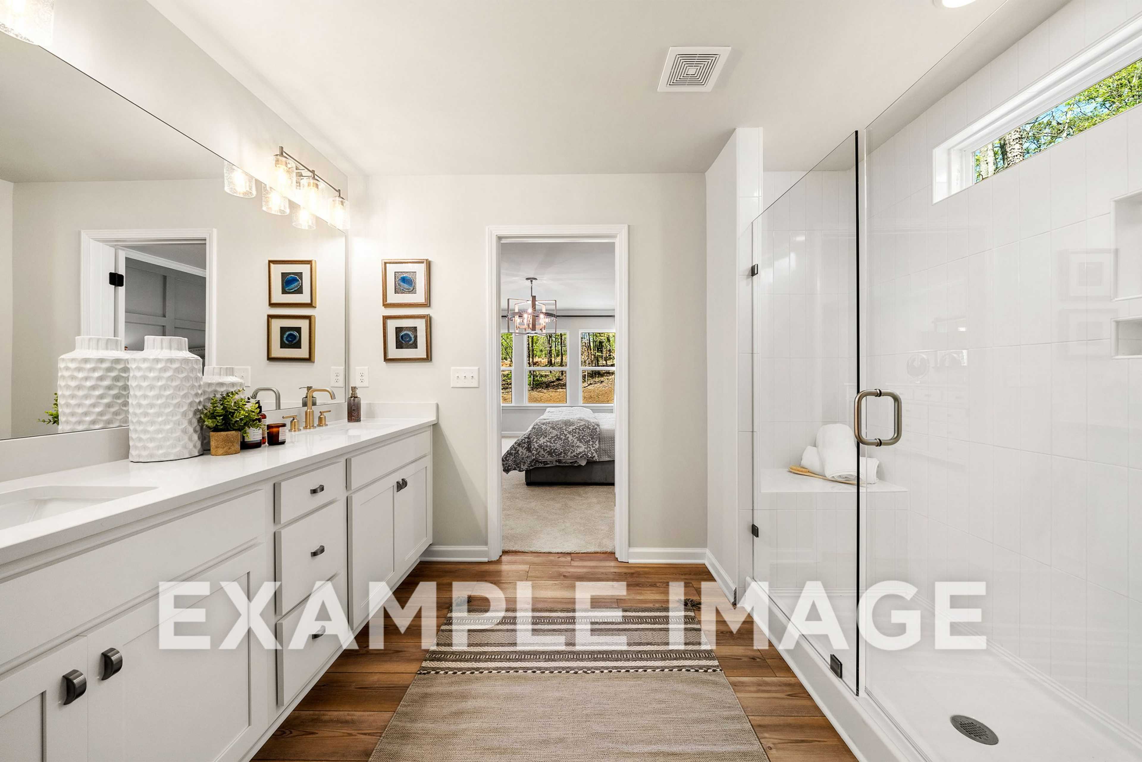 Modern master bathroom in The Hickory A featuring double white vanity, glass shower, and hardwood floors