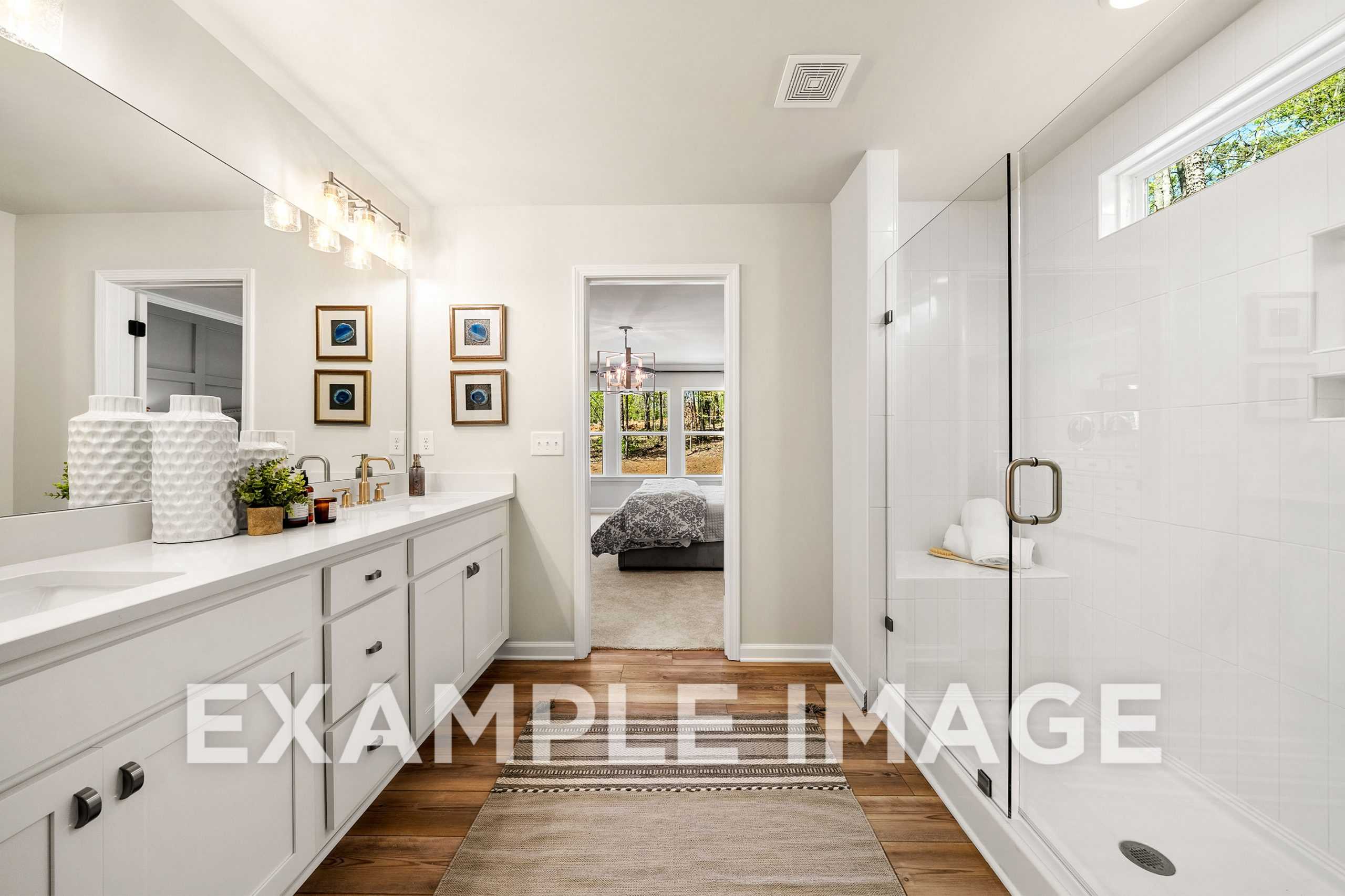 Modern master bathroom in The Hickory A featuring double white vanity, glass shower, and hardwood floors