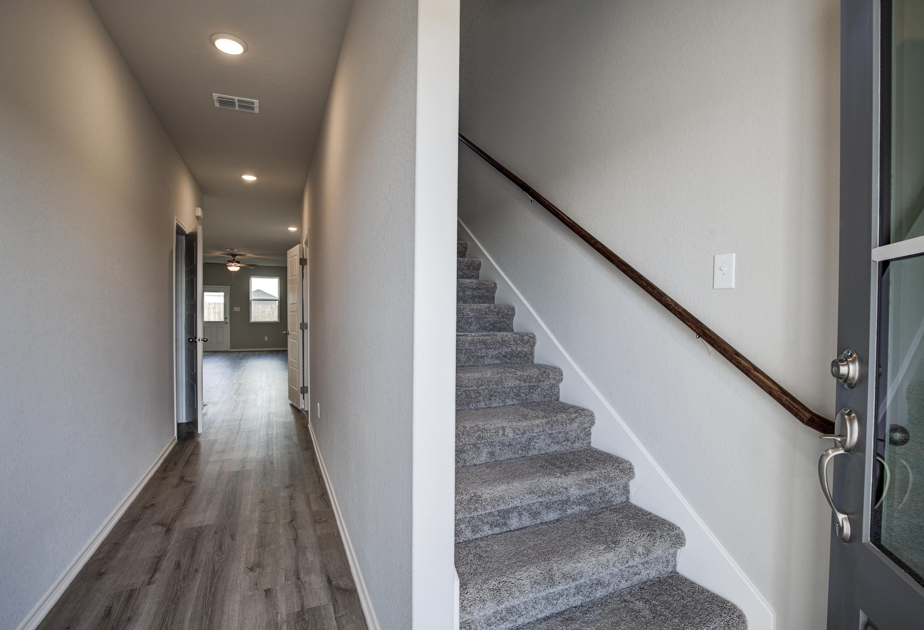 Spacious hallway with luxury vinyl plank flooring and carpeted staircase in The Blanco A 2-story home by Davidson Homes