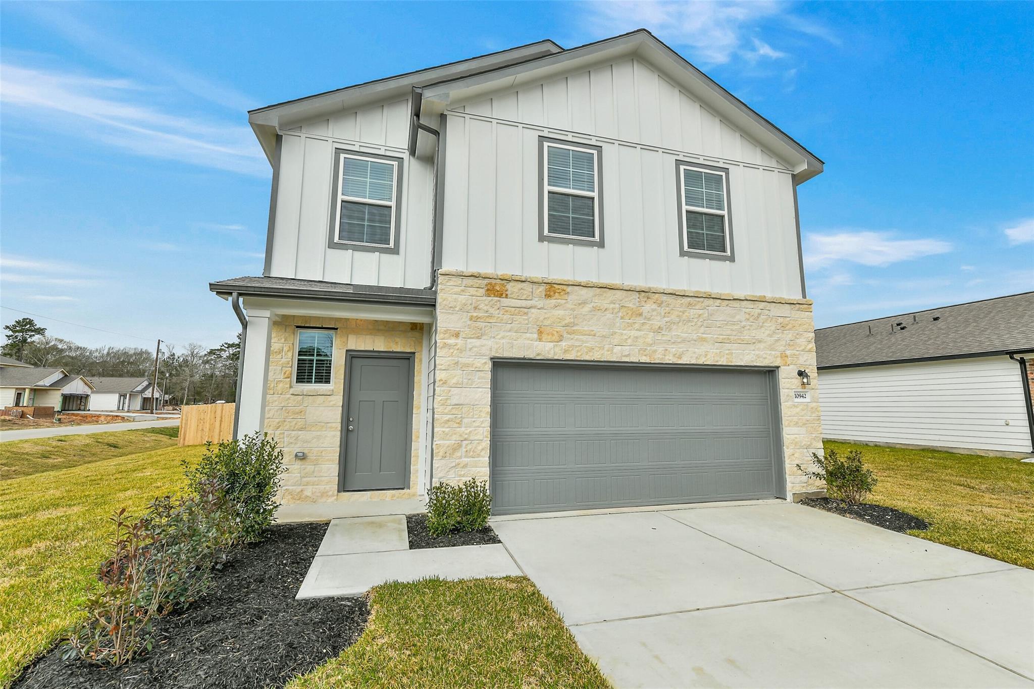 Modern two-story white home with stone accents, 2-car garage, and landscaped front yard in Liberty Estates, Cleveland, Texas