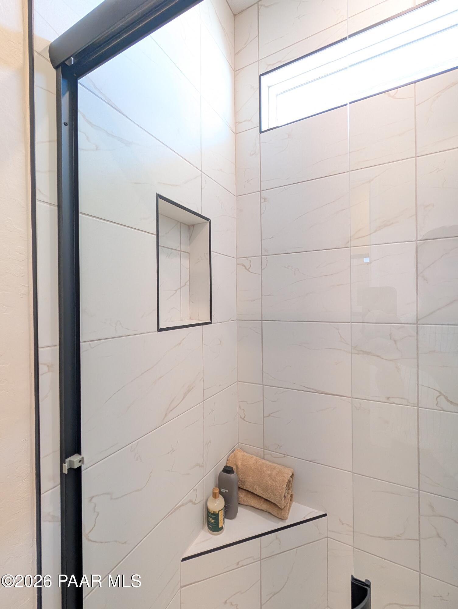 Walk-in shower with marble-look tile, built-in niche, and bench seat in The Boulder II H, South Ranch, Prescott, Arizona.