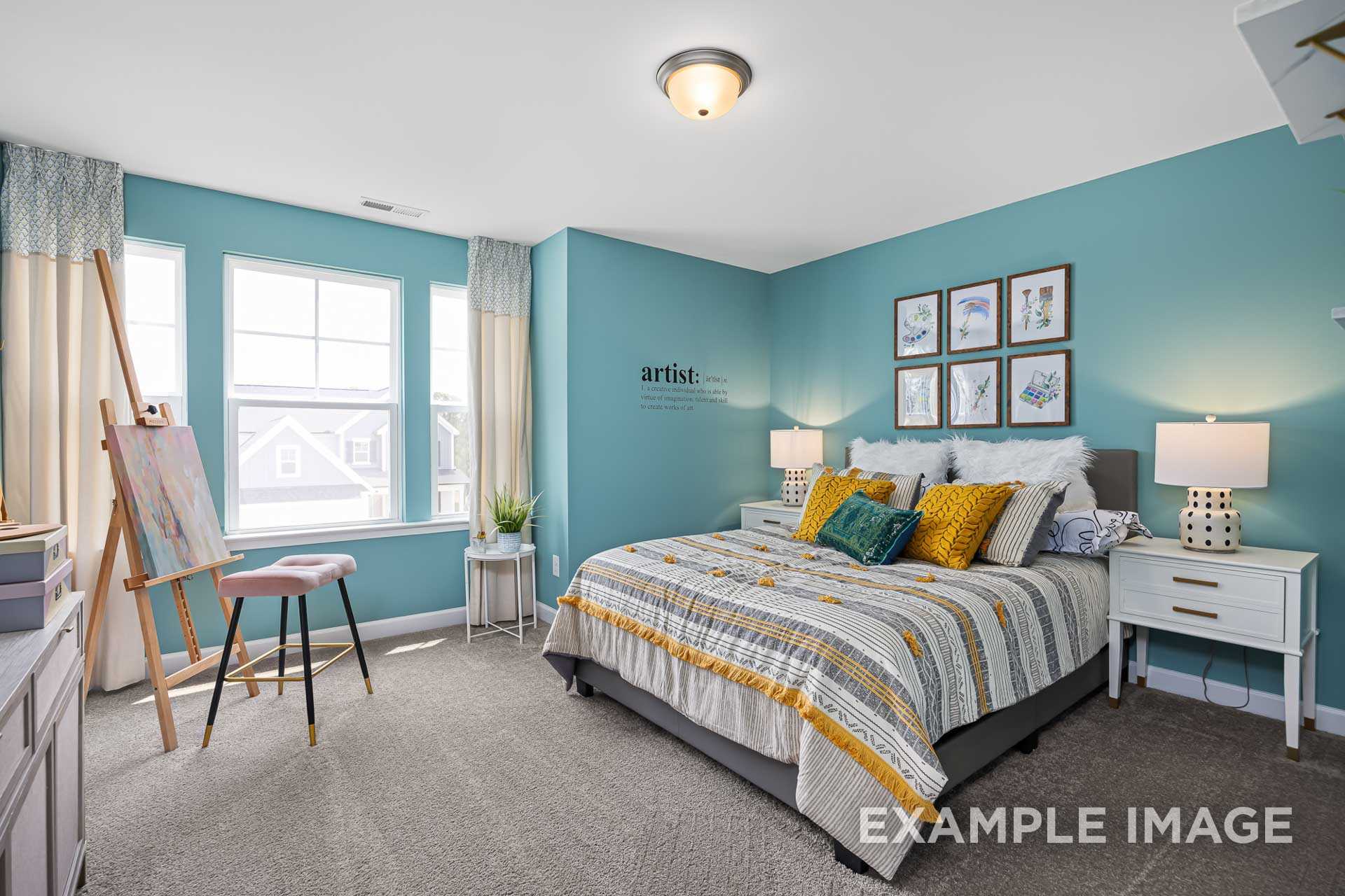 Spacious master suite in The Adalynn A with teal walls, king bed in gray-yellow bedding, art easel, pillows, lamps, and window