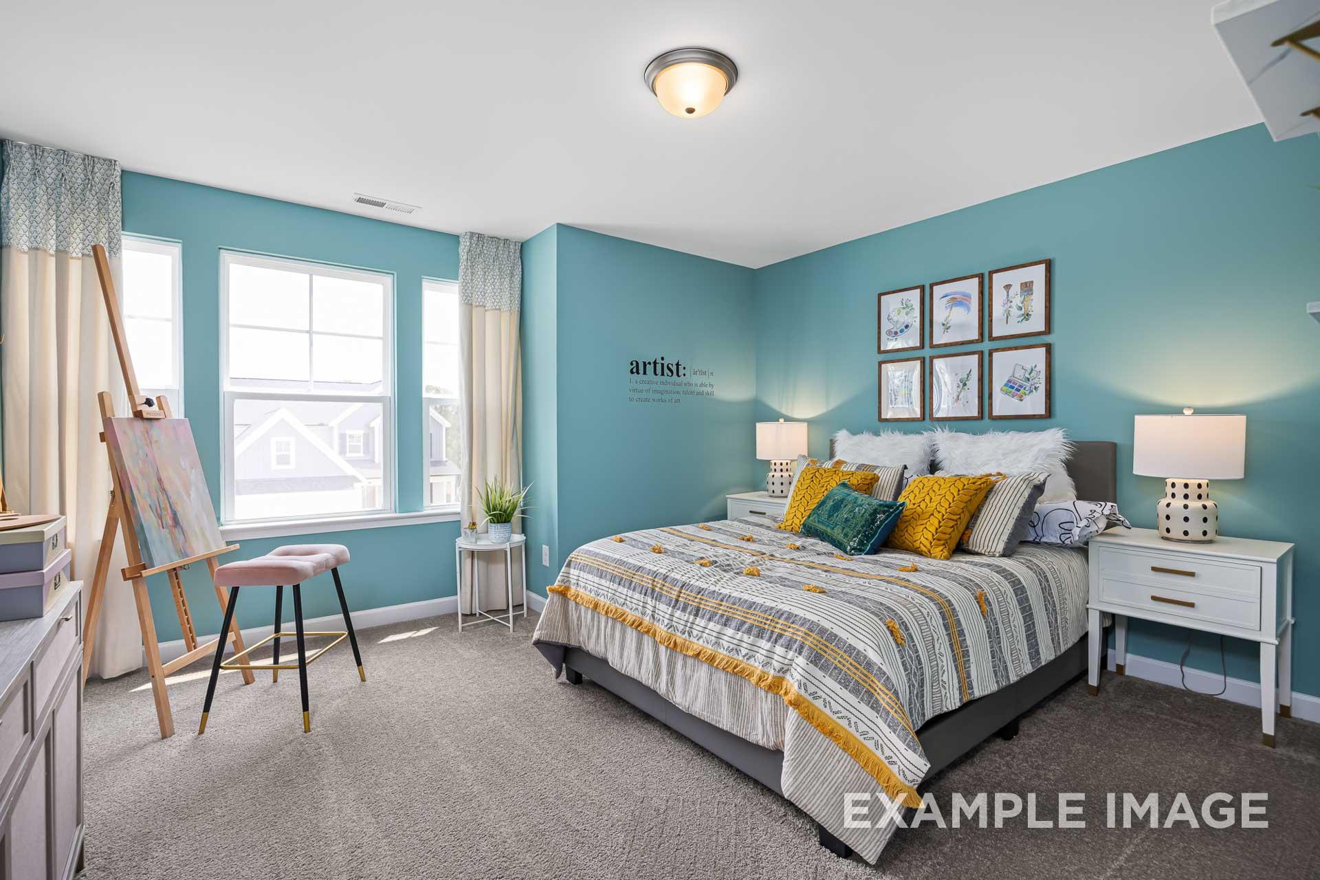 Spacious teal master bedroom in The Adalynn C with king bed, yellow pillows, artist's easel, and window views