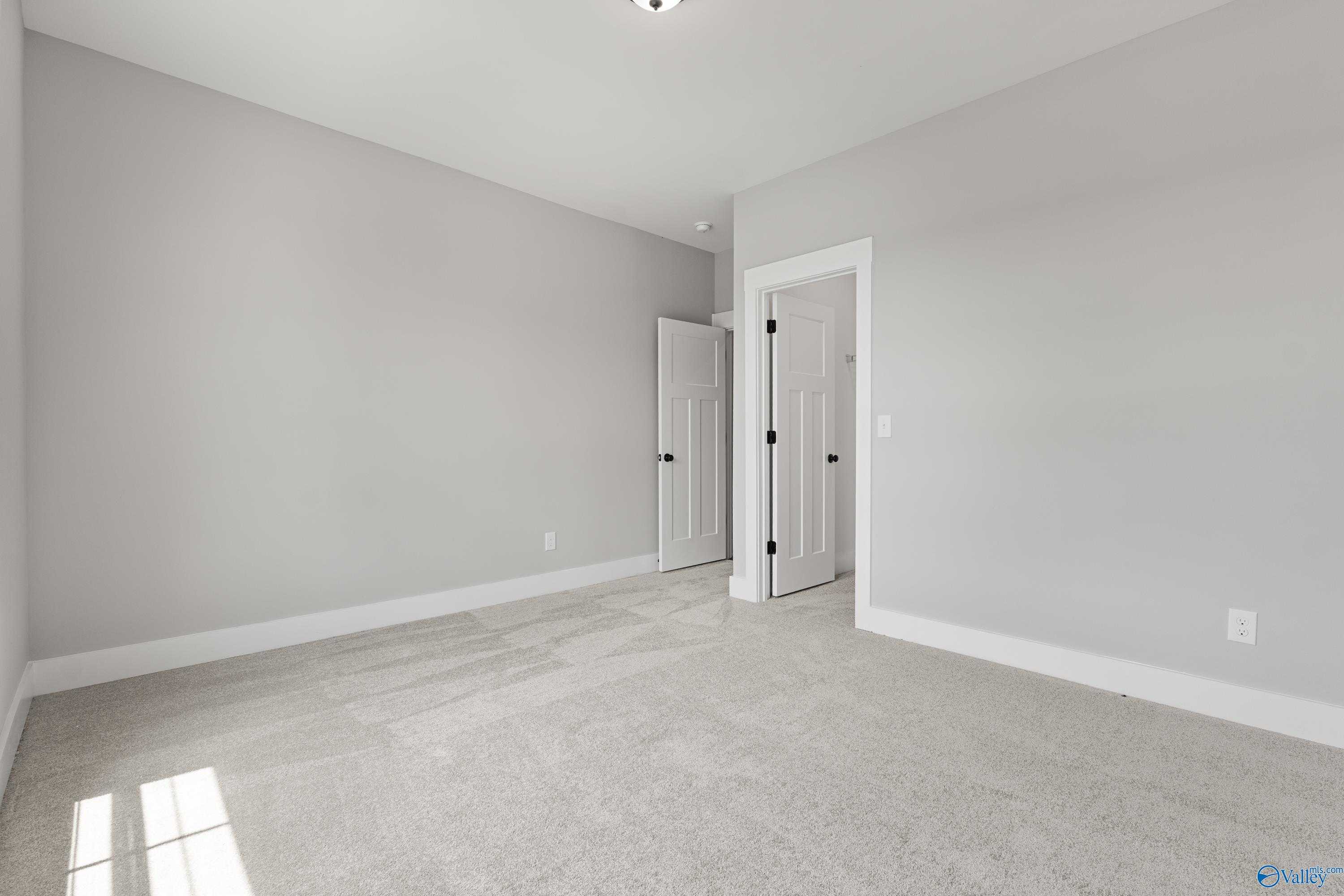Spacious empty bedroom with light gray walls, plush carpet, and adjacent doors in Davidson Homes The Arcadia, Huntsville AL