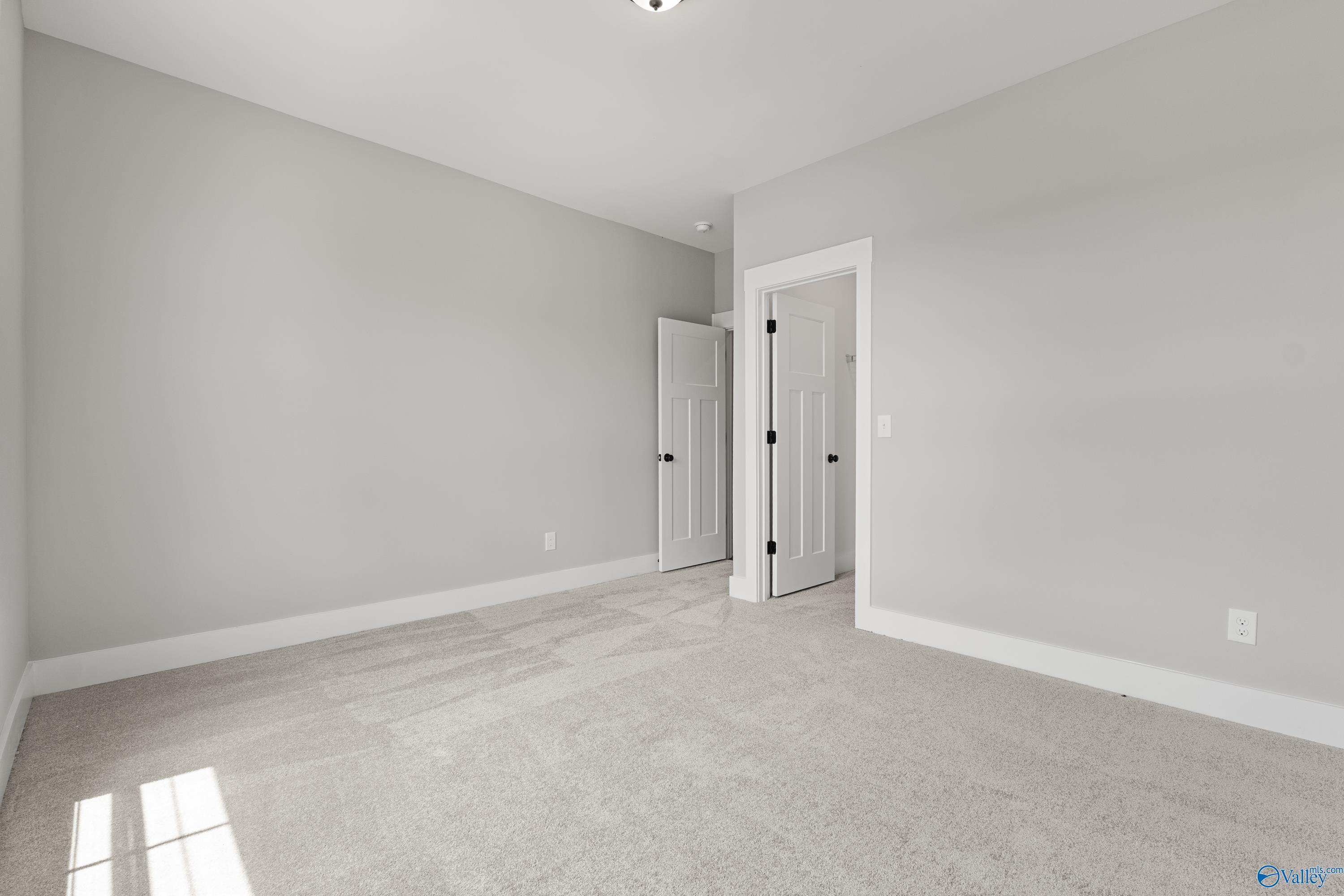 Spacious empty bedroom with light gray walls, plush carpet, and adjacent doors in Davidson Homes The Arcadia, Huntsville AL