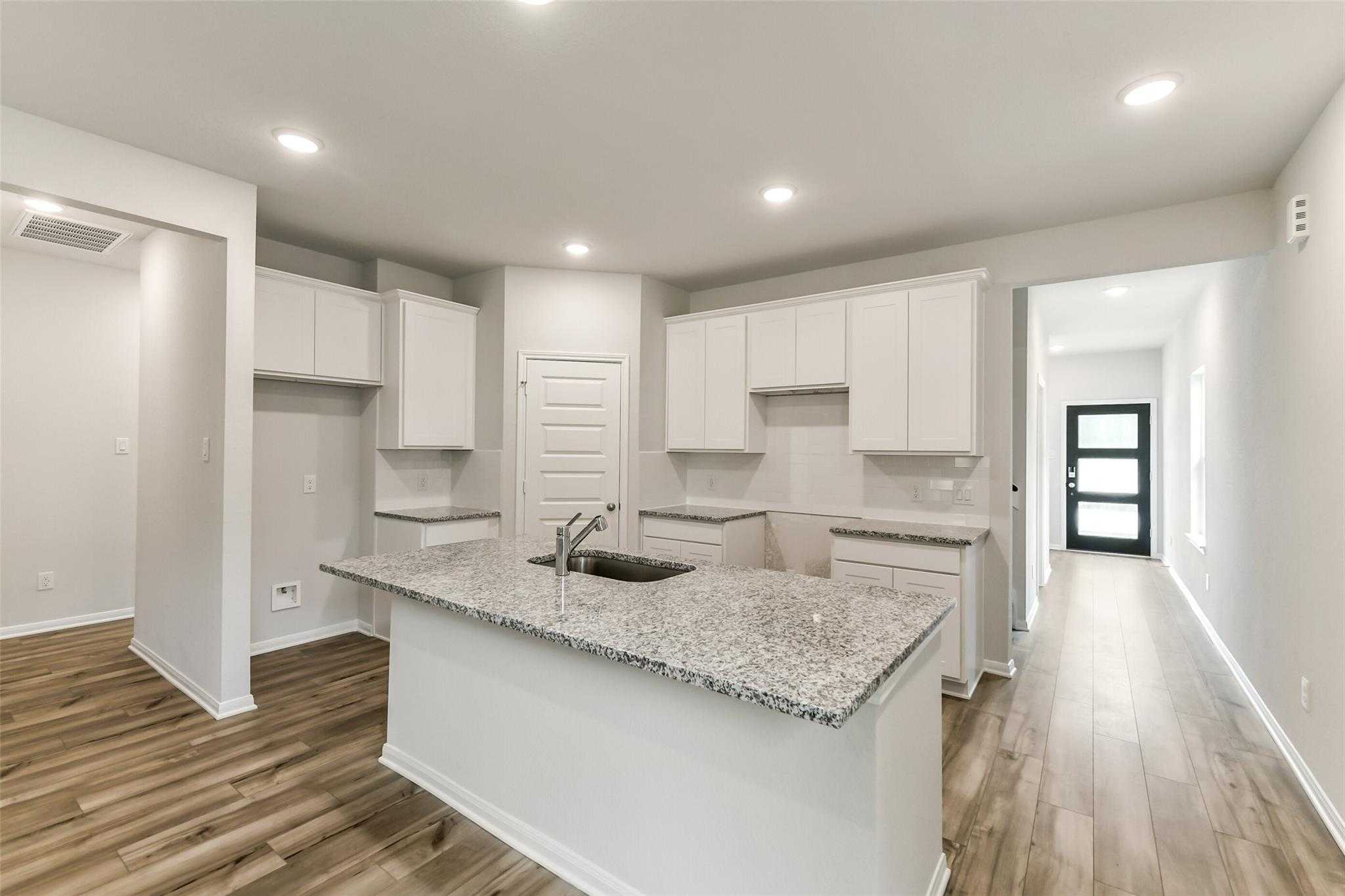Modern white kitchen with granite island sink, recessed lights, hardwood floors in Davidson Homes The Sabine F, Conroe, Texas