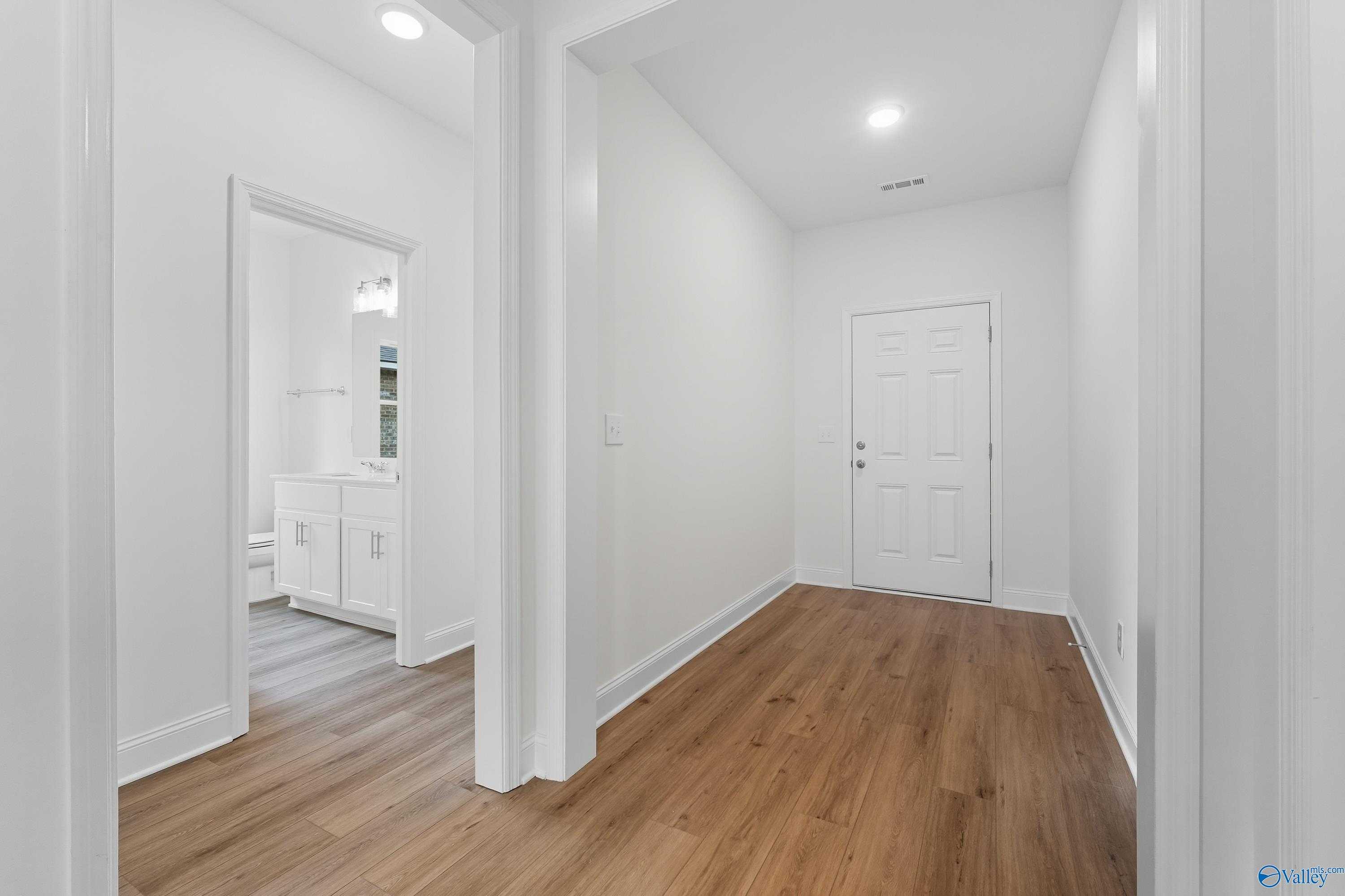 Bright hallway with luxury vinyl plank flooring, white walls, and guest bathroom vanity in The Everett 4-bedroom home, Meridianville, Alabama