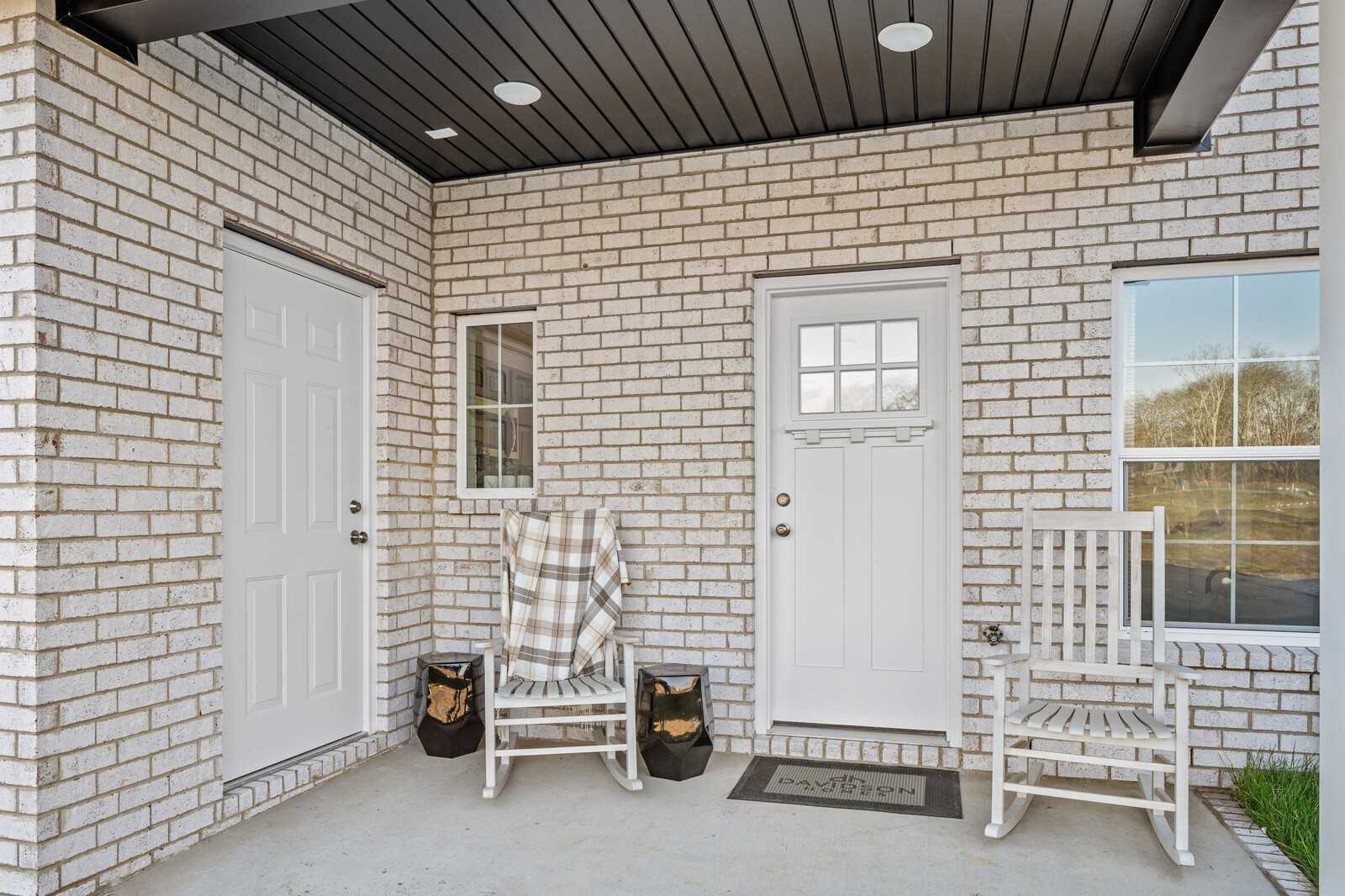 Inviting covered front porch with white brick exterior, rocking chairs, and plaid blankets in Davidson Homes Cumberland A, Gallatin, TN