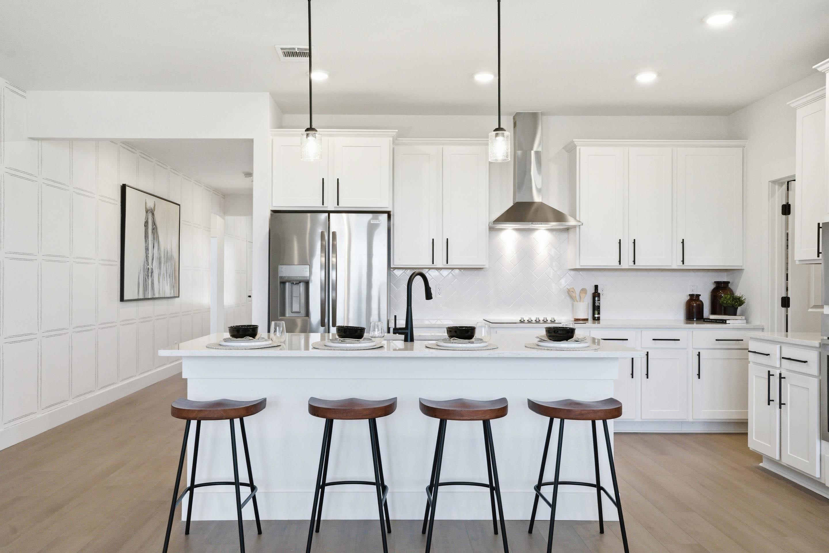 Modern white kitchen in The Laurel featuring a spacious island, pendant lighting, stainless steel appliances, and wall trim.