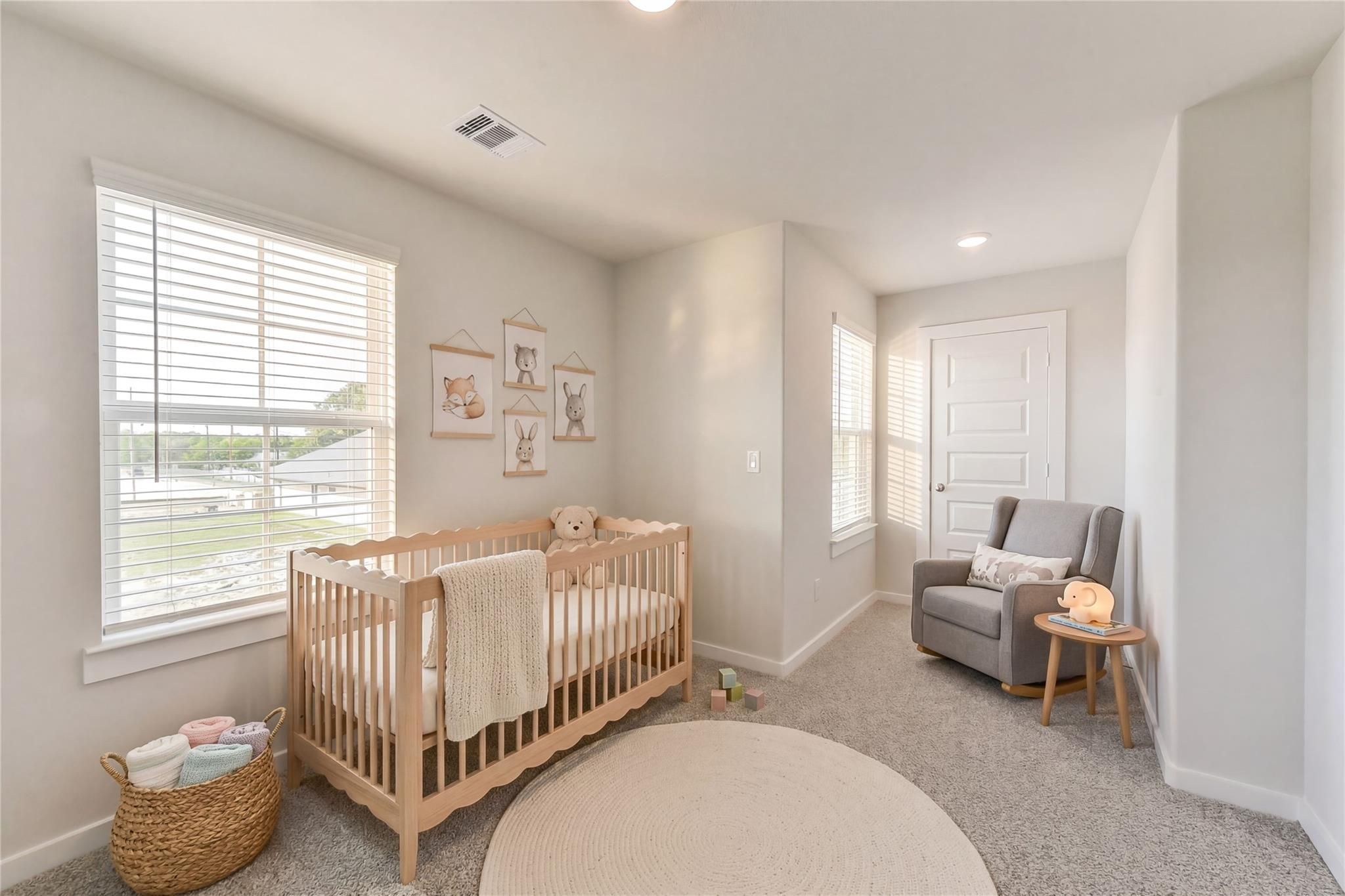 Cozy nursery featuring white crib, gray rocking chair, round rug, and bunny artwork in 5-bedroom Davidson Homes The Brazos E, Magnolia, Texas